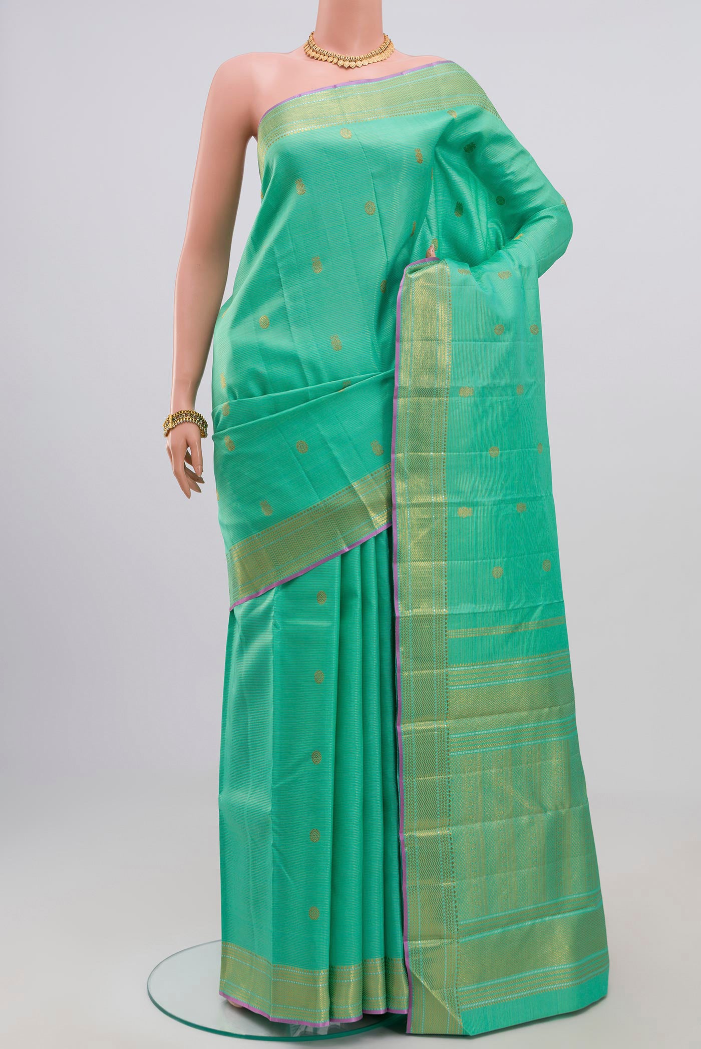 Green Kanjivaram Saree with Zari Butta on the body and Zari Border.  displayed on a mannequin