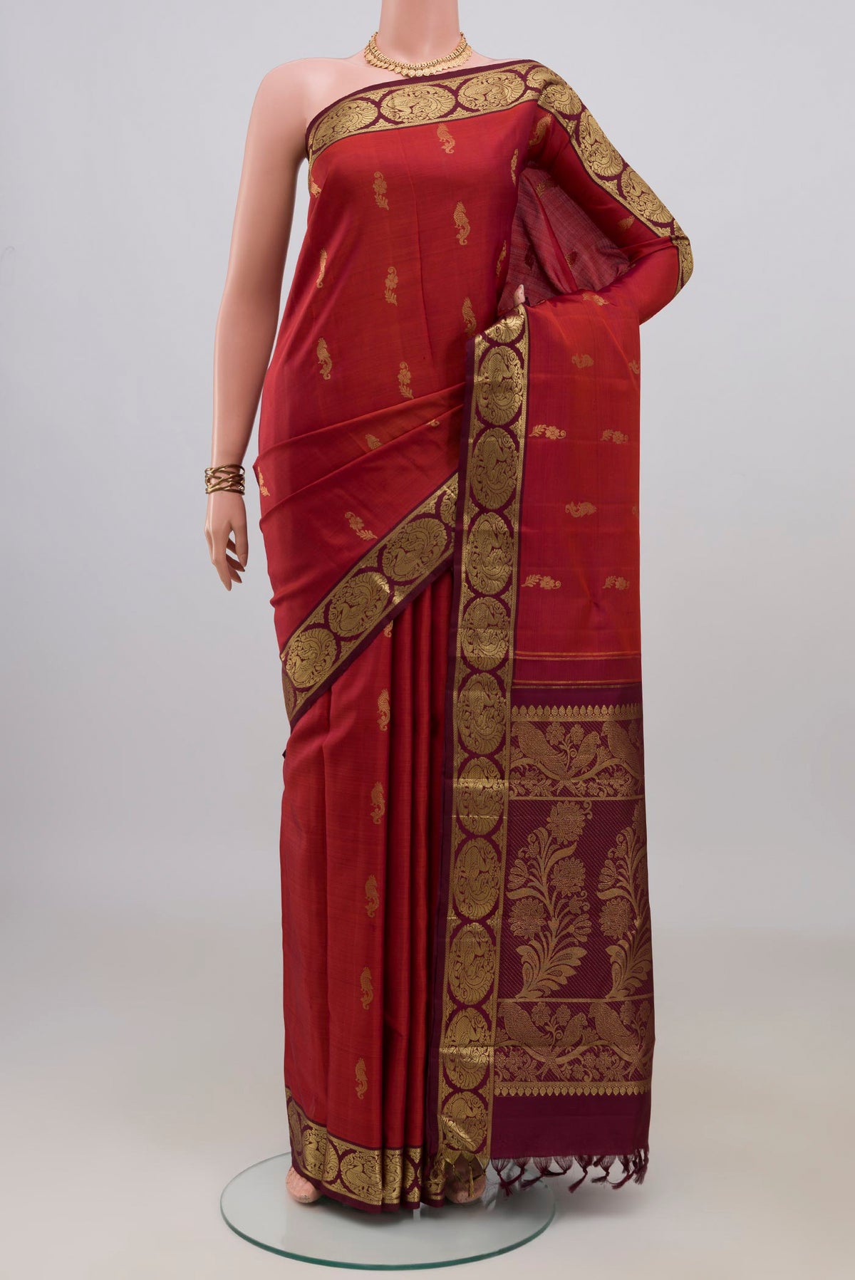 Pure Silk Rust Kanchipuram Saree with Zari Butta on the body and Zari Border.  displayed on a mannequin