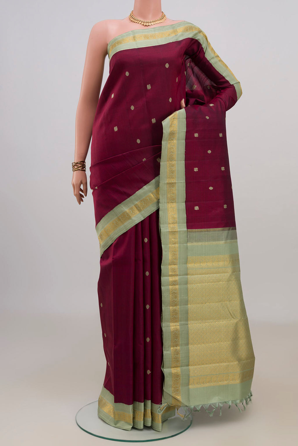 Pure Silk Maroon Kanjivaram Saree with Thread Butta on the body and Zari Border.  displayed on a mannequin