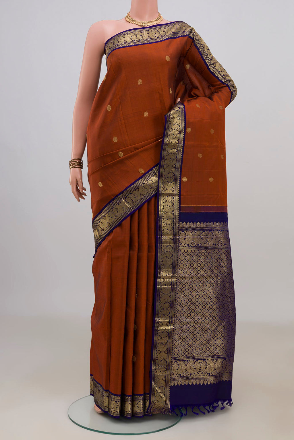 Pure Silk Rust Kanjivaram Saree with Zari Butta on the body and Zari Border.  displayed on a mannequin