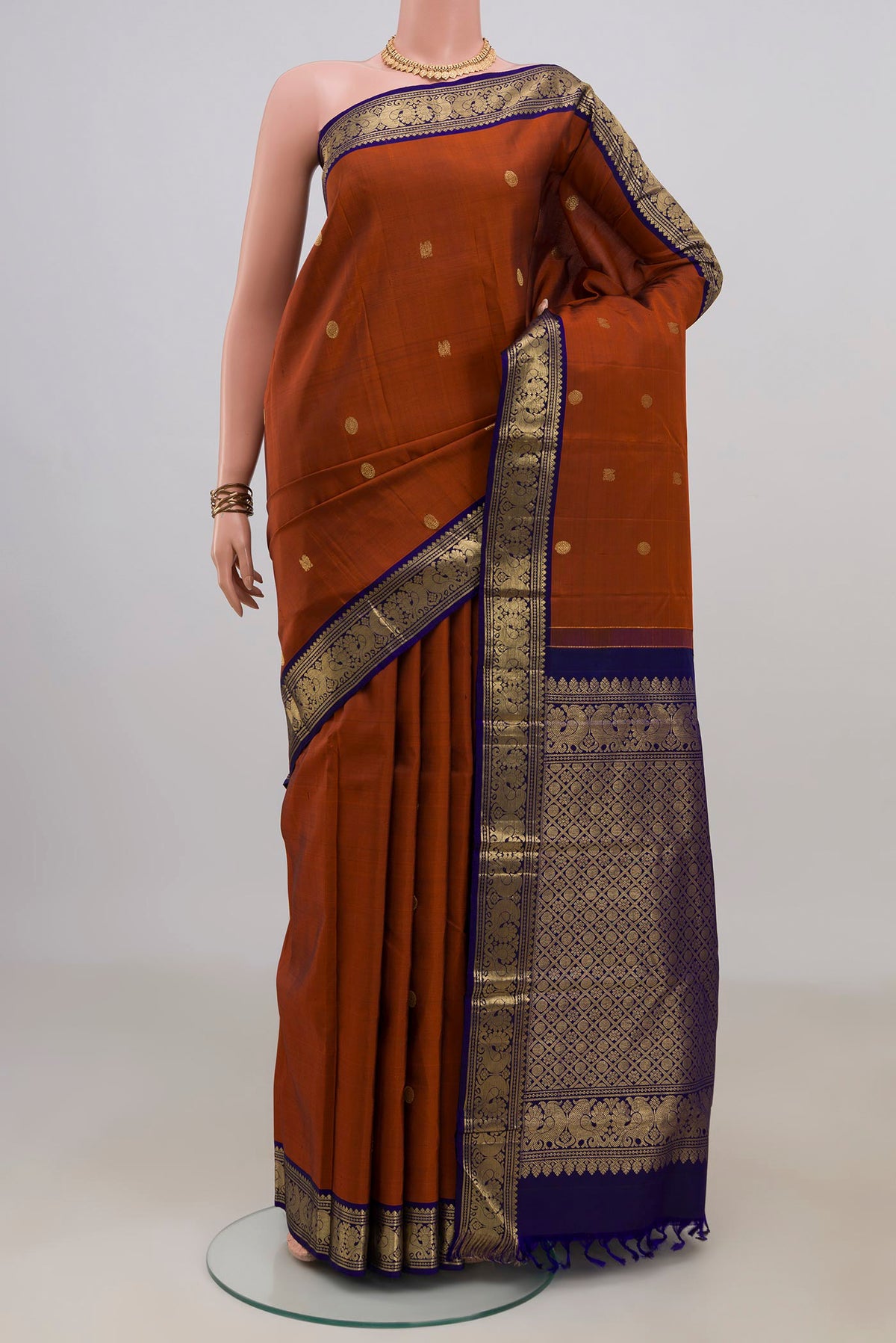 Pure Silk Rust Kanjivaram Saree with Zari Butta on the body and Zari Border.  displayed on a mannequin