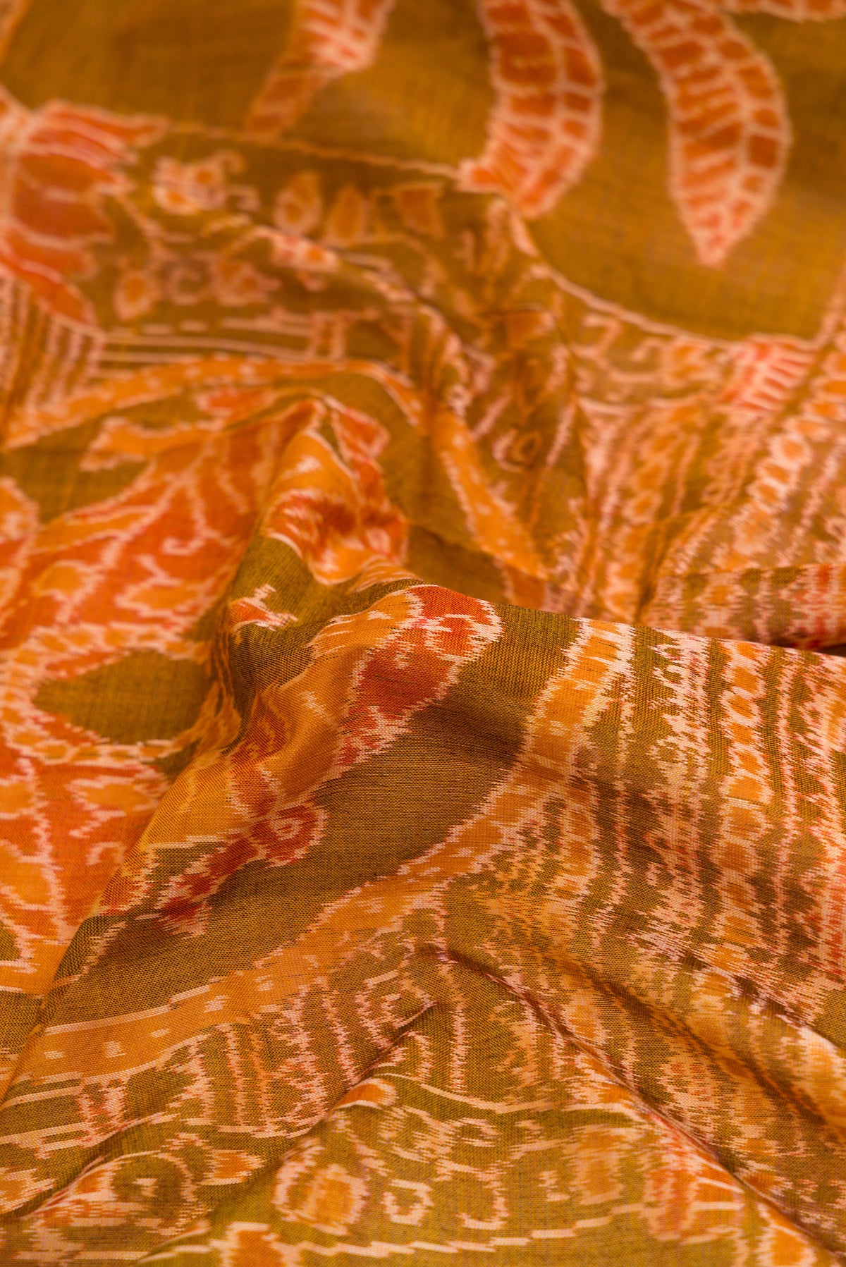 Close up of Mustard Dual Tone Double Ikat Saree with Ikat Print on the body and Thread Border.  displaying folds
