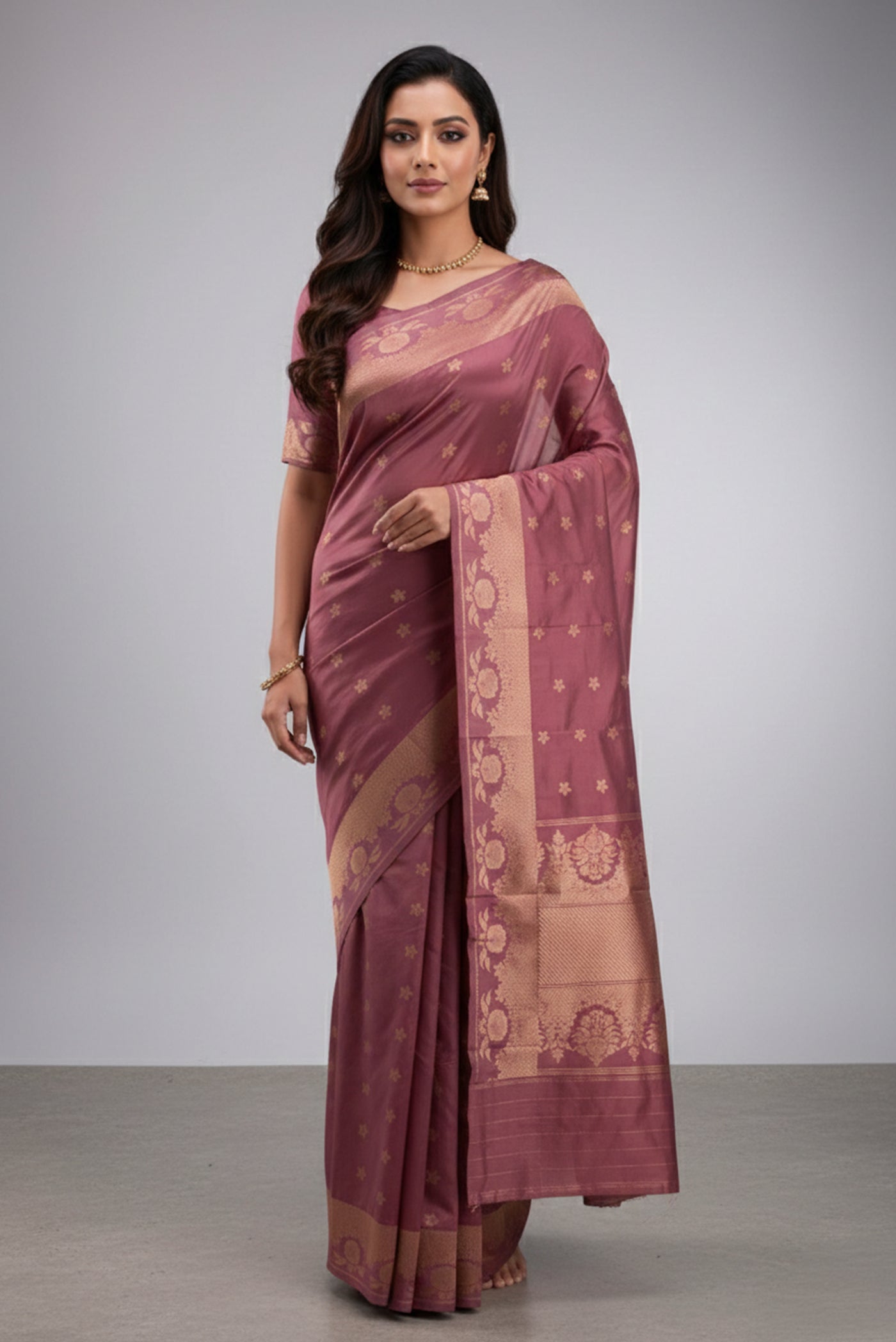 Model wearing a Gulal, handwoven in Katan silk with gold zari, is crafted using the phekwa technique, allowing closely spaced motifs to emerge with precision. Tiny floral butis in a dense half-step repeat lend the body a soft, textured richness. Art Nouveau?inspired floral arches define the borders, each framing a complementary buta, while a solid gold twill pallu completes the saree with depth and classic balance.