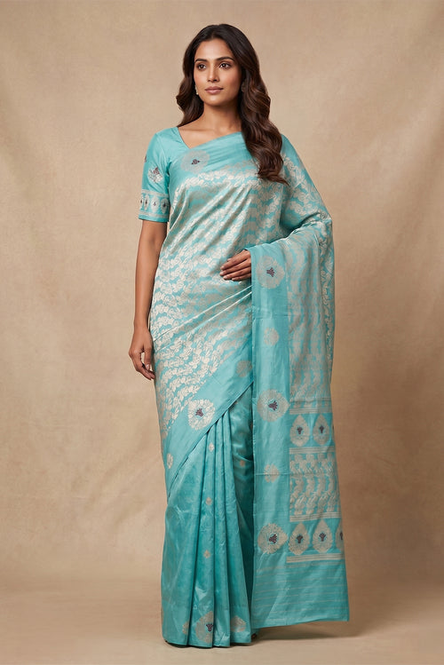 Model wearing a Anaar, woven in silk with a satin border, highlights the intricacy of kadhua weaving accented with meenakari. Designed in a half-and-half layout, the saree features delicate pomegranate butas on one half and a flowing pomegranate jaal on the other. Alternating satin border motifs and a jaal-led pallu, divided by a row of butas, lend rhythm and balance, drawing from the organic stylisation of Art Nouveau.