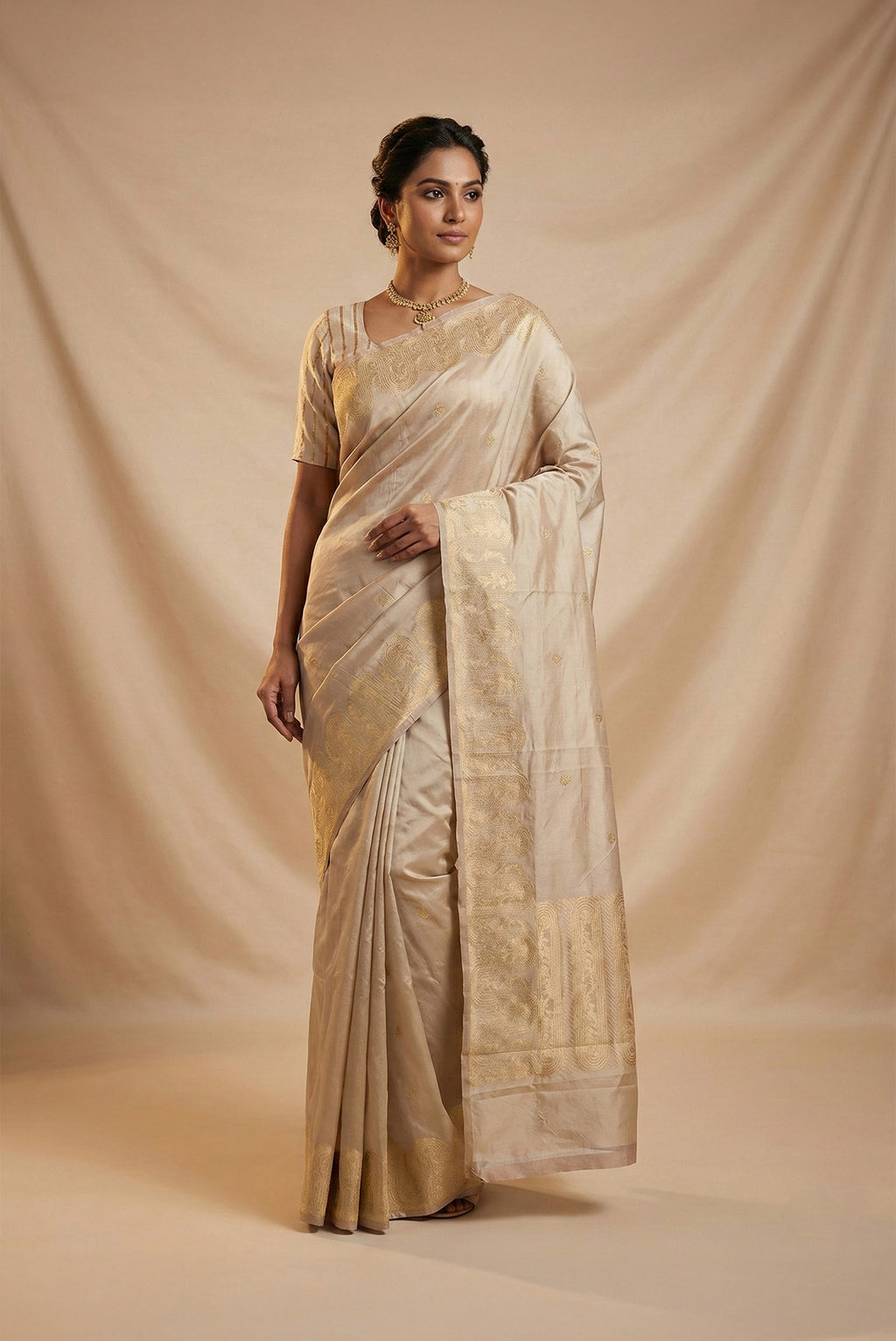 Model wearing a Mandhara, handwoven in Katan silk, brings together kadhua weaving and delicate meenakari detailing Crafted in gold zari with silver accents, the saree draws from Art Nouveau florals and the concentric forms of Dhokra metal craft Wavy, concentric borders with floral vines frame the design, while tiny silver-meenakari butis dot the body The pallu completes the saree with elongated floral panels, lending a balanced, composed finish