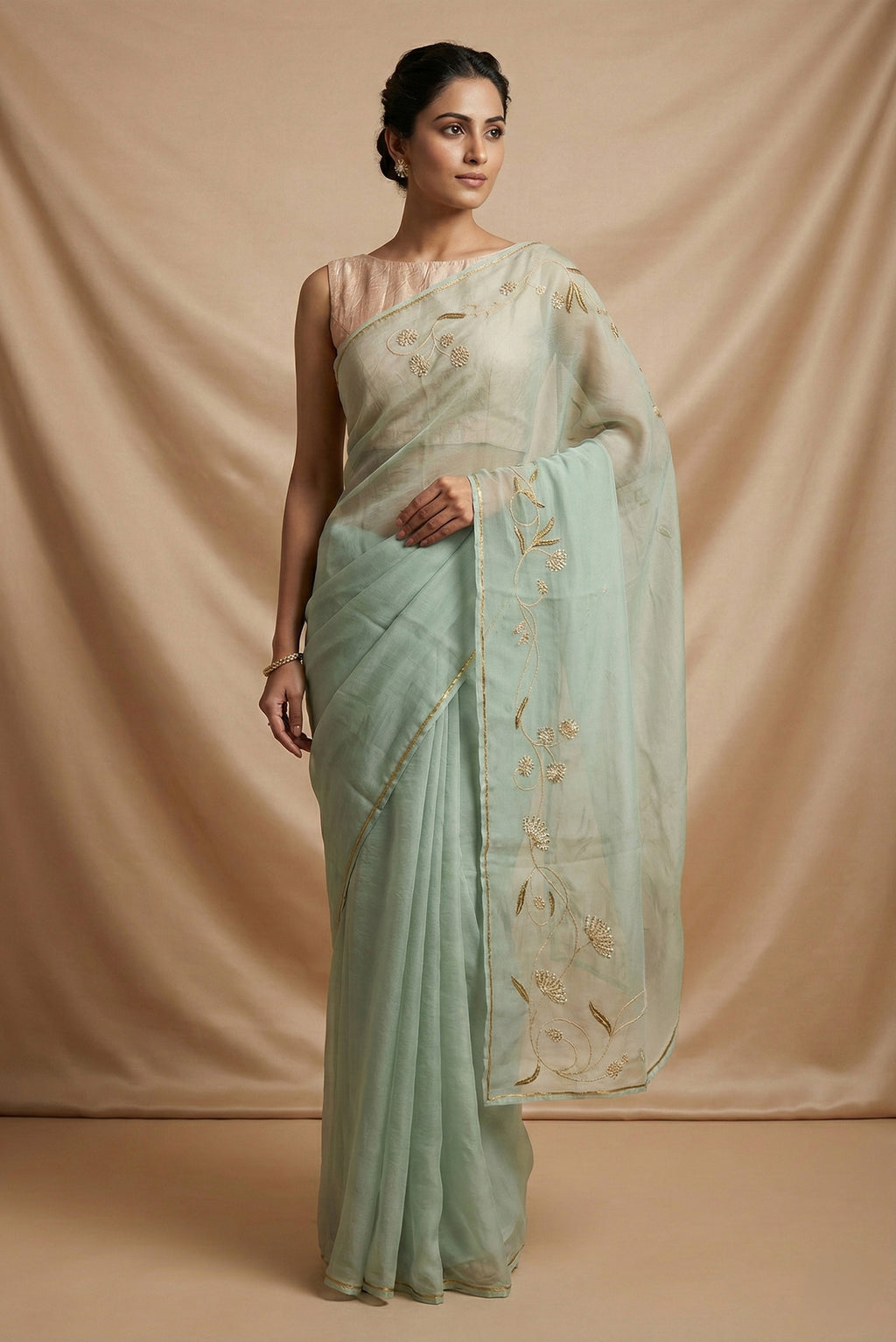 Model wearing a Bahar, crafted in silk organza, features delicate pani-zari enriched with zardozi, gota work, and dabka embroidery Its defining element is an off-center floral vine running vertically through the body, breaking symmetry with quiet intent Inspired by Art Nouveau?s flowing lines, the vine is rendered in slender leaves, zari chain-stitched stems, and alternating gota and zardozi flowers The pallu trails gently onto the body in scattered embroidered blooms