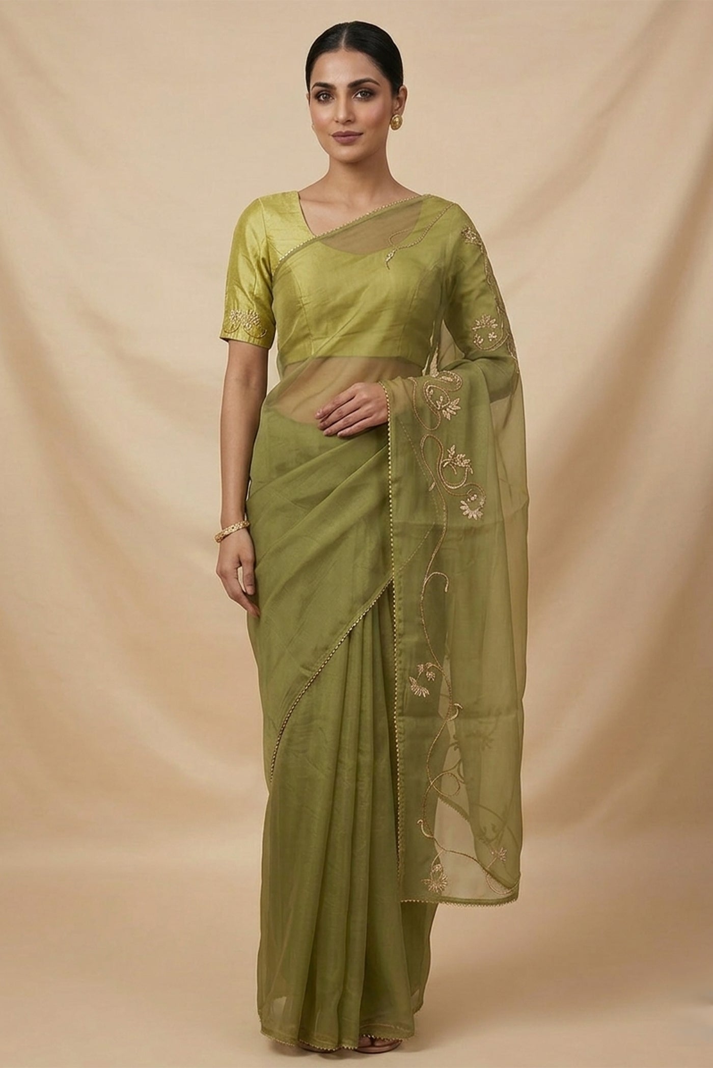Model wearing a In Mira, pure silk organza becomes a canvas for antique gold and pani zari, brought to life through fine dabka and aari embroidery. The pallu takes inspiration from the bull masks of the Cameroon Grasslands, translating their powerful curves into graceful motifs layered with florals and Art Nouveau lines. Dual-tone zari and detailed shoulders lend the saree depth, movement, and a refined festive glow.