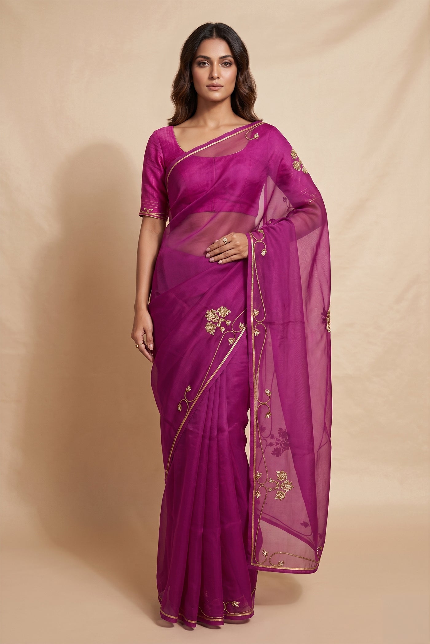Model wearing a Meher, crafted in silk organza, is hand-embroidered with gold and antique-gold zardozi. Organic vines and floral buds form a rich border that meets at a delicate fan motif - an ornamental form celebrated in late 19th and early 20th century Art Nouveau design. Iris flowers, symbolising femininity, grace, and mystique, echo the saree?s fluid curves as the motif repeats across the body, finished with elegant gota edges.