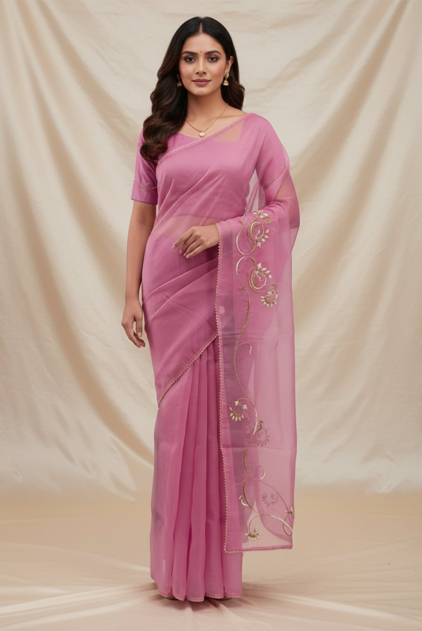 Model wearing a In Mira, pure silk organza becomes a canvas for antique gold and pani zari, brought to life through fine dabka and aari embroidery. The pallu takes inspiration from the bull masks of the Cameroon Grasslands, translating their powerful curves into graceful motifs layered with florals and Art Nouveau lines. Dual-tone zari and detailed shoulders lend the saree depth, movement, and a refined festive glow.