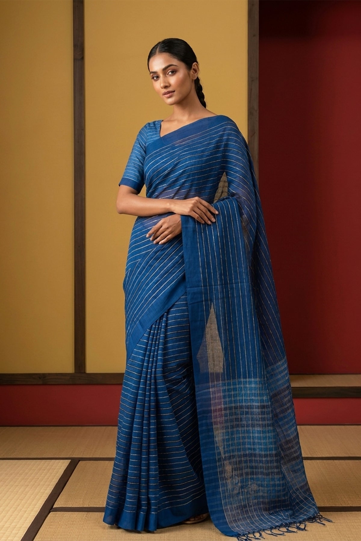 Model wearing a Mishri, a celebration of summer in Bengal cotton, is woven in fine 60-count cotton and drapes with natural comfort. Soft stripes move in gentle linear patterns across the fabric, creating a lively yet balanced design. The fine checks they form are a gentle reminder of crystal sugar, lending the saree its name. Light, breathable, and effortlessly wearable for sunlit days.