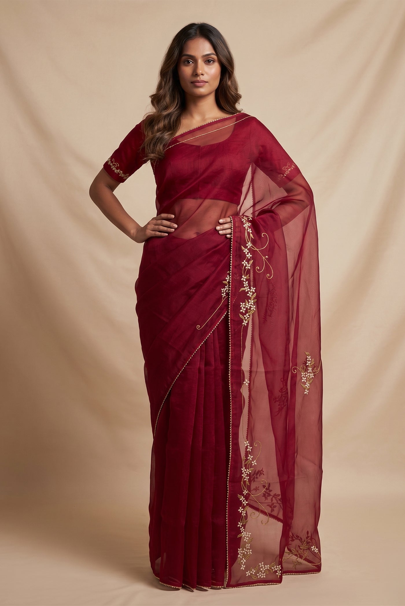 Model wearing a Mahira organza saree is inspired by the hydrangea blooms of the Art Nouveau movement. Along the border and edges, bold, simplified hydrangea blooms pair with fluid, curving stems. The flowers gain soft dimension through pani-zari zardozi, while antique-gold aari embroidery adds depth and balance. The pallu features three large asymmetrical butas, formed as flowing clusters of hydrangea blooms and stems, creating a graceful focal point.