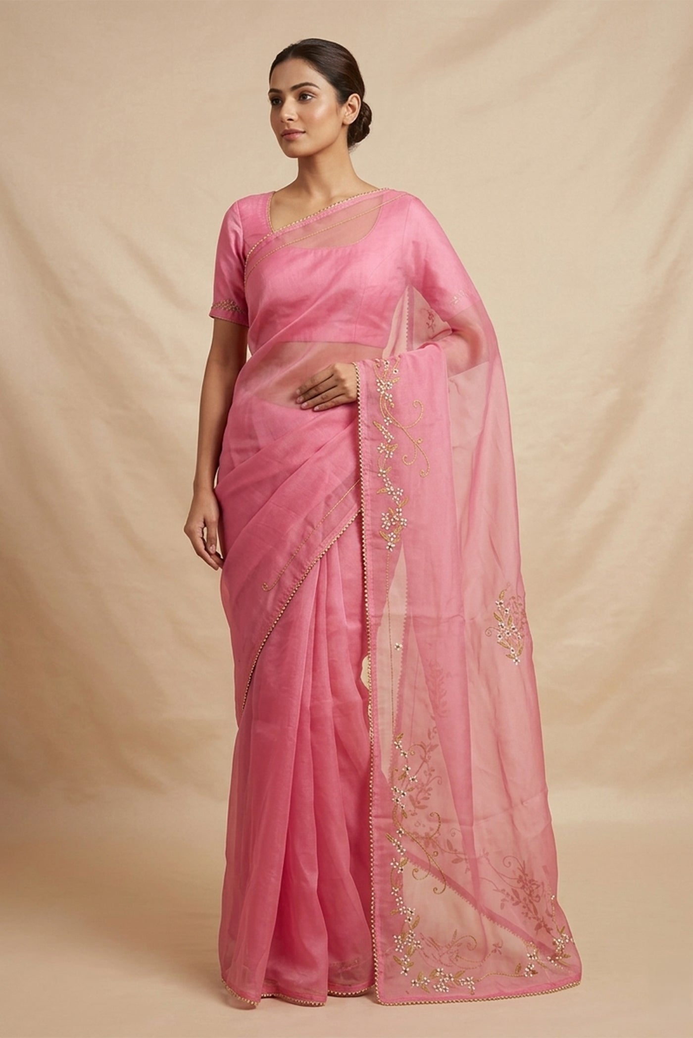 Model wearing a Mahira organza saree is inspired by the hydrangea blooms of the Art Nouveau movement. Along the border and edges, bold, simplified hydrangea blooms pair with fluid, curving stems. The flowers gain soft dimension through pani-zari zardozi, while antique-gold aari embroidery adds depth and balance. The pallu features three large asymmetrical butas, formed as flowing clusters of hydrangea blooms and stems, creating a graceful focal point.
