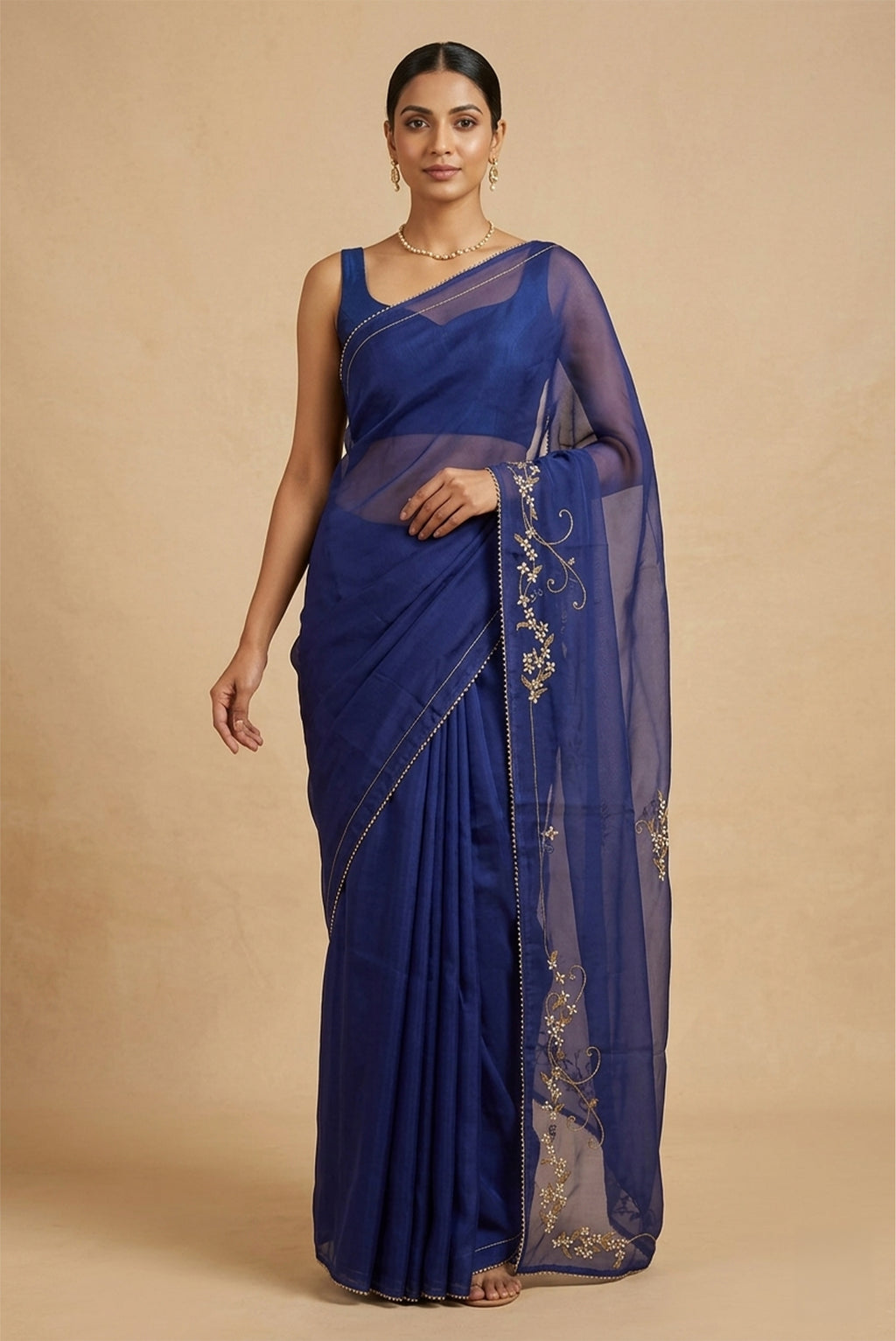 Model wearing a Mahira organza saree is inspired by the hydrangea blooms of the Art Nouveau movement. Along the border and edges, bold, simplified hydrangea blooms pair with fluid, curving stems. The flowers gain soft dimension through pani-zari zardozi, while antique-gold aari embroidery adds depth and balance. The pallu features three large asymmetrical butas, formed as flowing clusters of hydrangea blooms and stems, creating a graceful focal point.