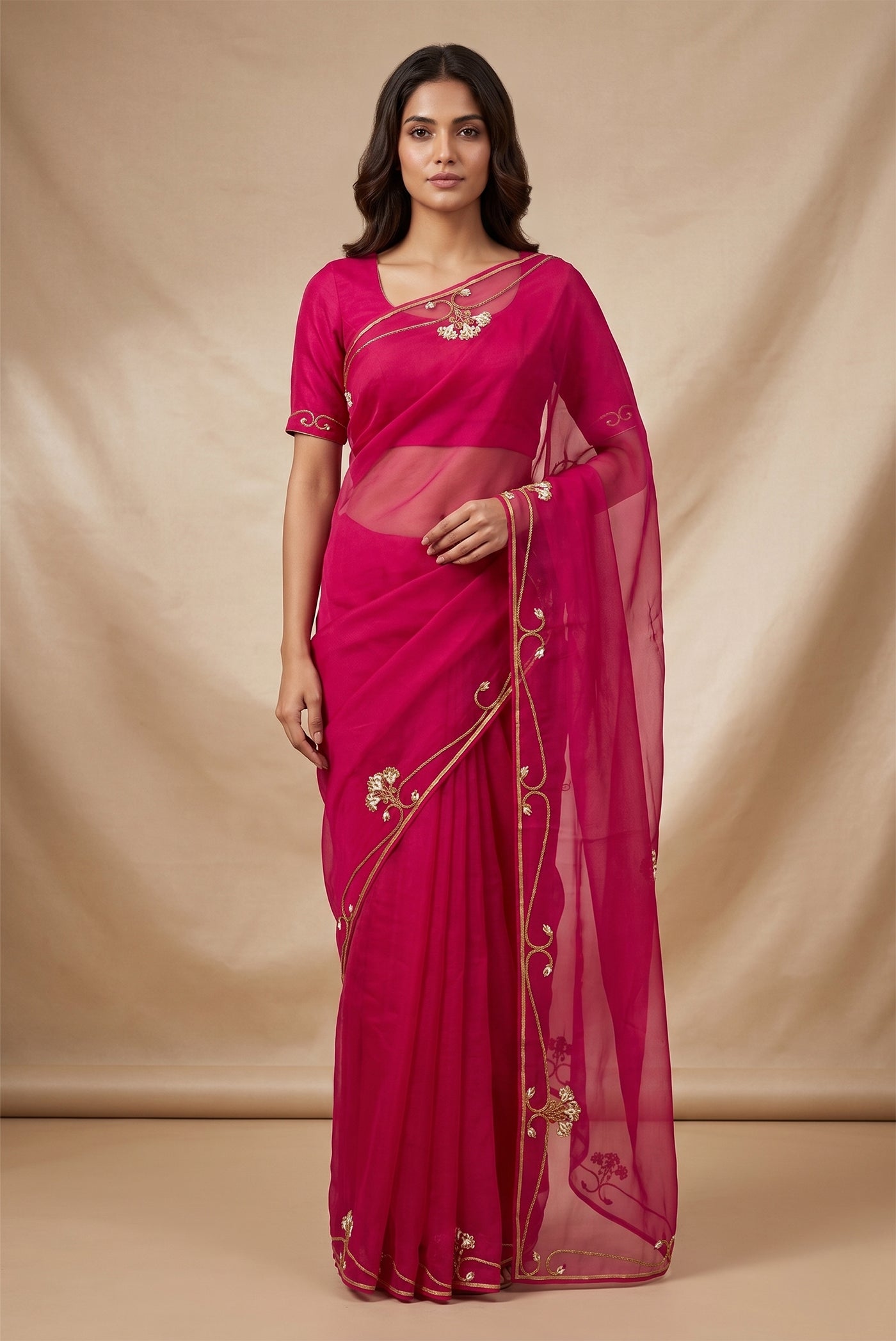 Model wearing a Meher, crafted in silk organza, is hand-embroidered with gold and antique-gold zardozi. Organic vines and floral buds form a rich border that meets at a delicate fan motif - an ornamental form celebrated in late 19th and early 20th century Art Nouveau design. Iris flowers, symbolising femininity, grace, and mystique, echo the saree?s fluid curves as the motif repeats across the body, finished with elegant gota edges.