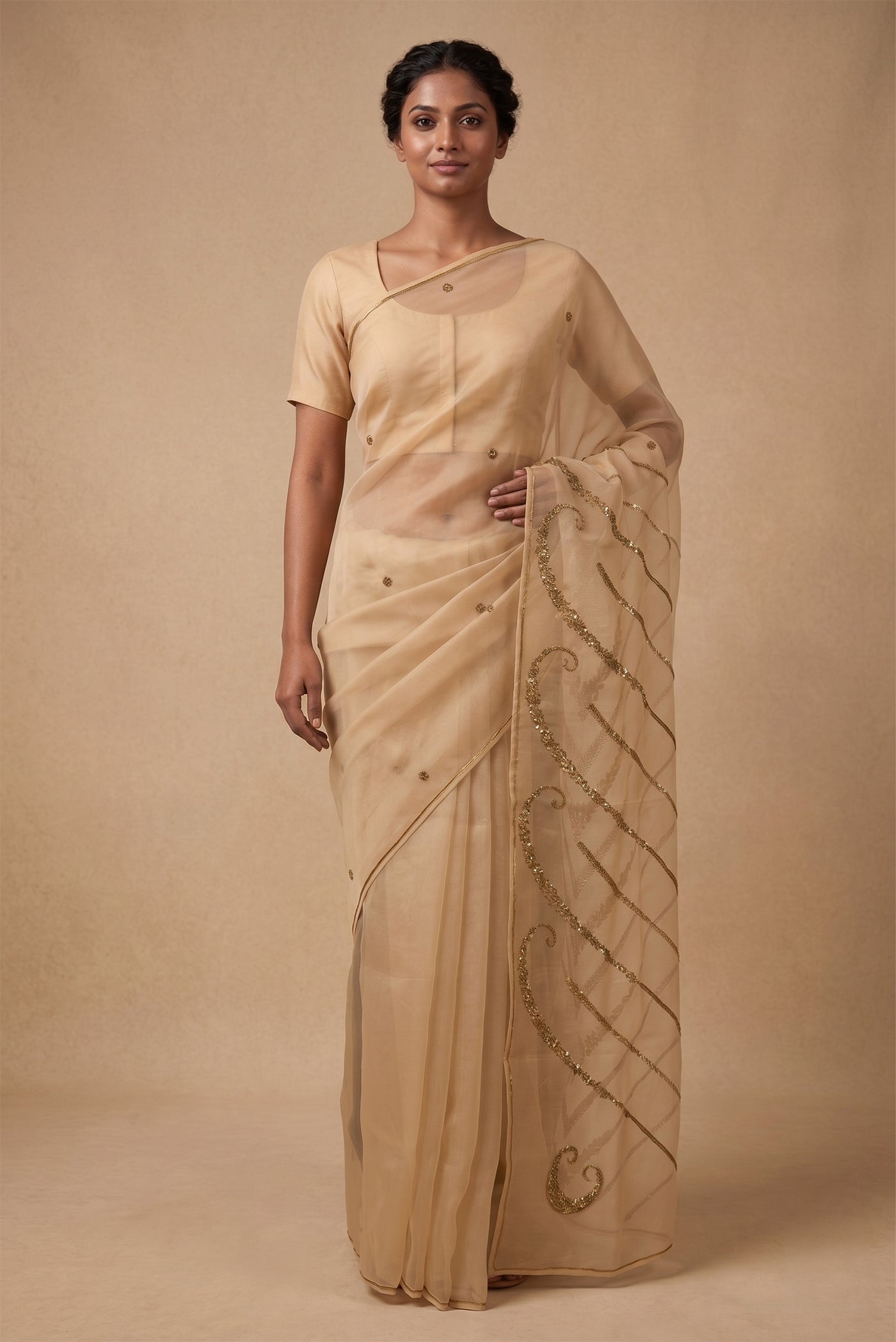Model wearing a Sitara, crafted in silk organza and embroidered in antique-gold zardozi, draws from Art Nouveau?s love for organic, nature-led forms and the graceful contours of butterfly wings. The pallu features striking V-shaped motifs filled with floral embroidery, worked in dabka, sequins, and beads, alternating between dense and lighter forms. A minimal floral body allows the statement pallu to unfold with soft grandeur.