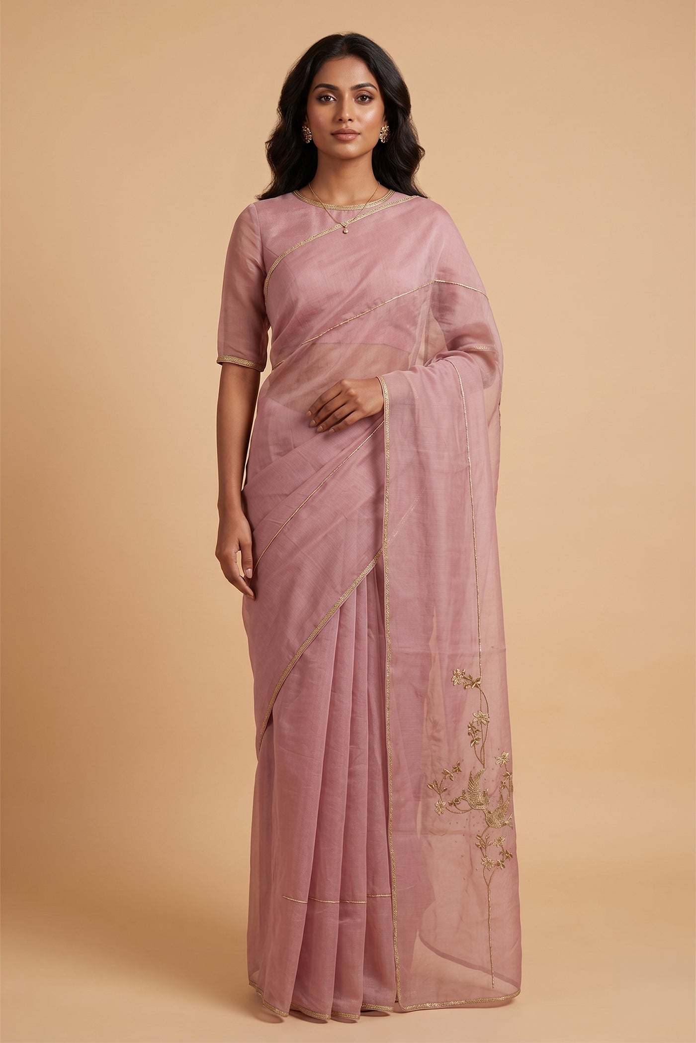 Model wearing a Bulbul draws from Art Nouveau florals and graceful natural forms. Crafted in cotton tissue with antique gold and pani-zari zardozi, it features delicate embroidered clusters of stylised sparrows perched on slender stems amid flowers. Thoughtfully placed across the saree, shoulder and pallu, these motifs create elegant rhythm, while beadwork, dabka detailing and herringbone lace complete the finish.
