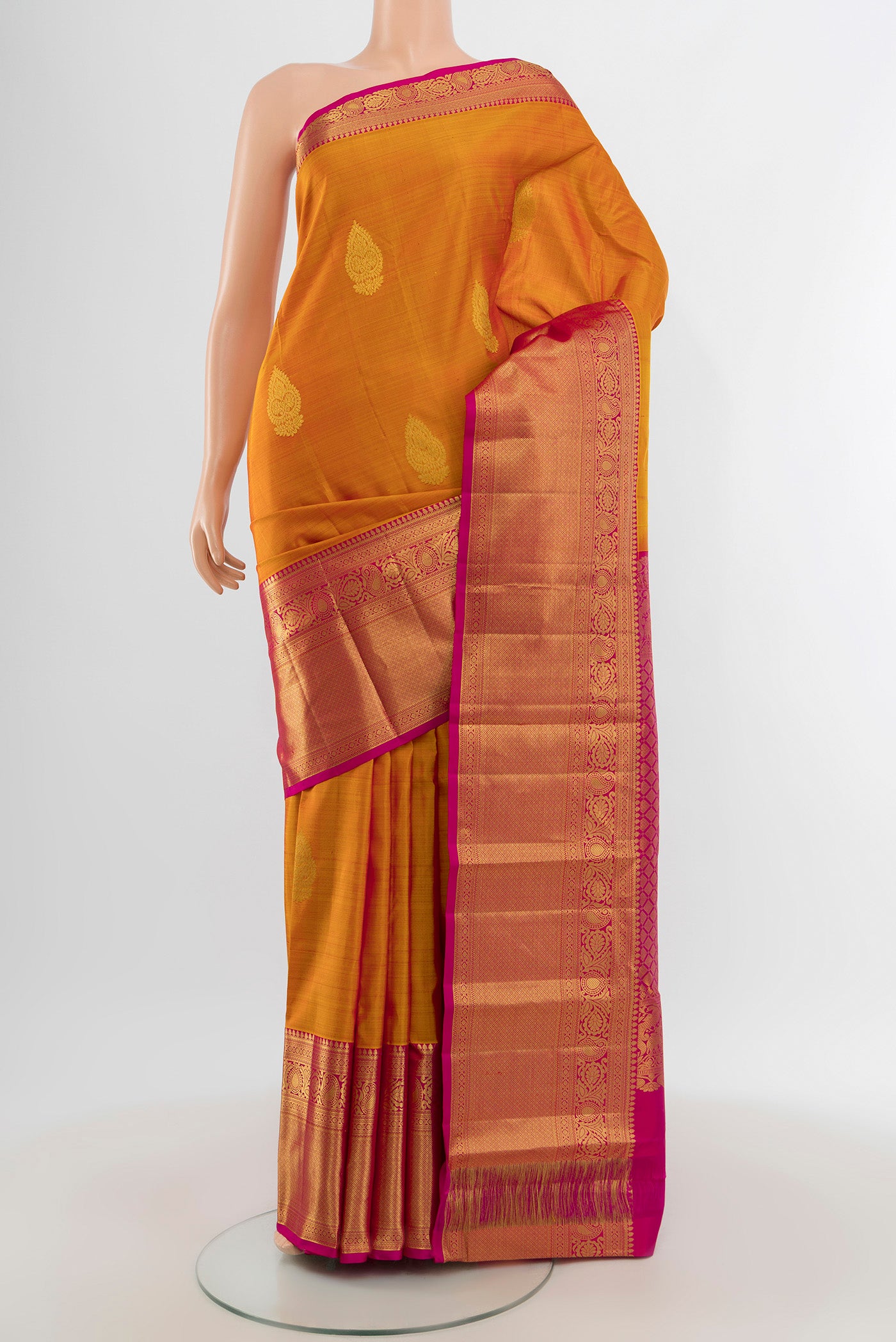Mustard Kanchipuram Silk Saree with Zari Butta on the body and Zari Border.  displayed on a mannequin