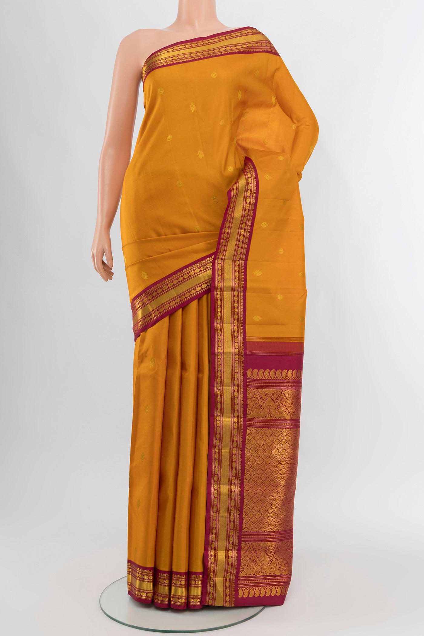 Mustard Kanchipuram Silk Saree with Zari Butta on the body and Zari Border.  displayed on a mannequin