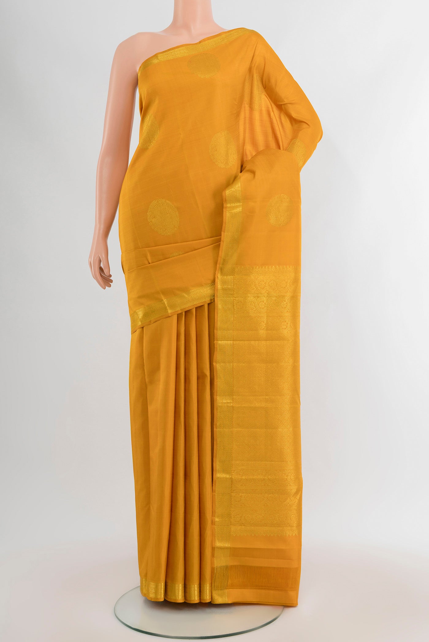 Mustard Kanchipuram Silk Saree with Zari Butta on the body and Zari Border.  displayed on a mannequin