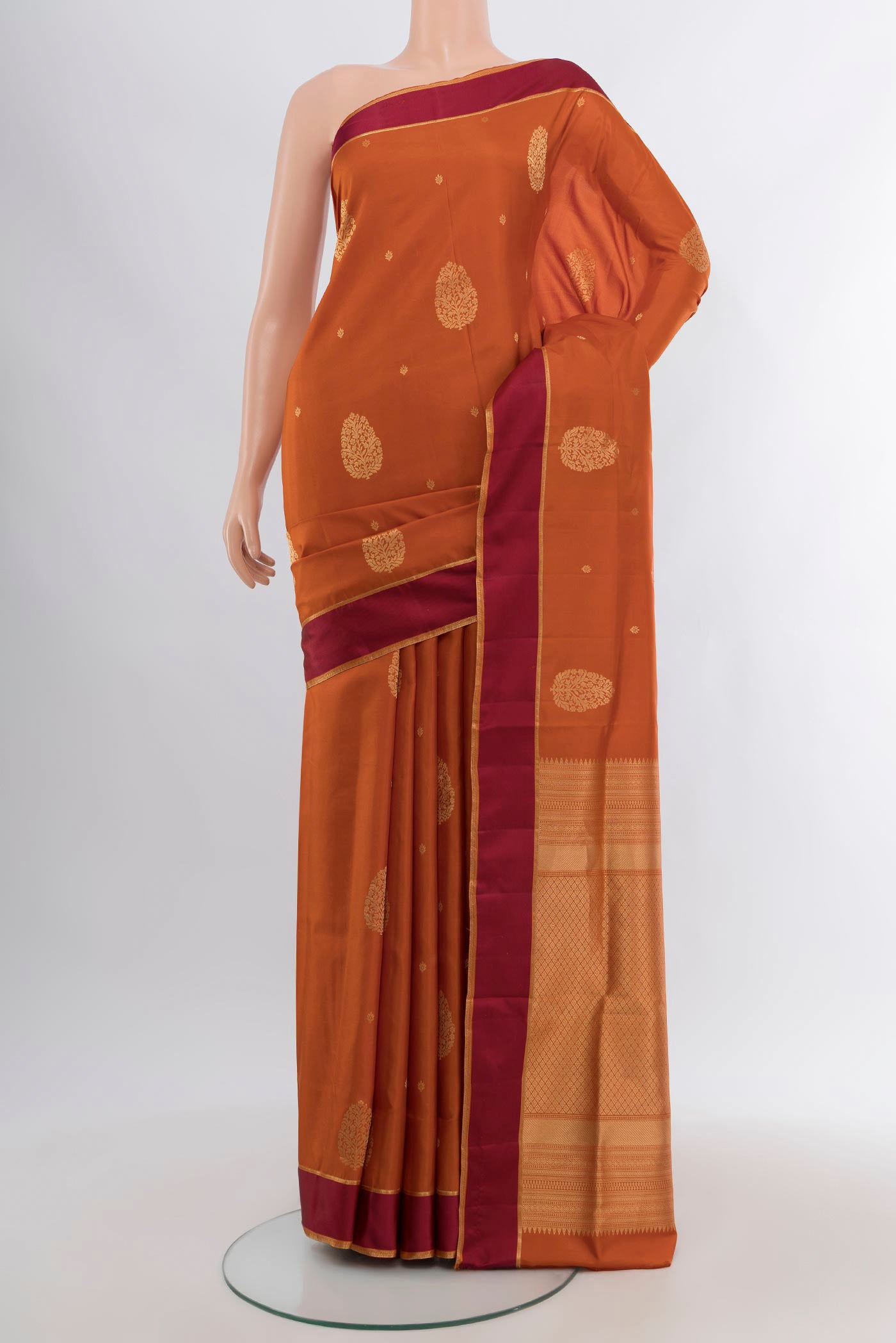 Rust Soft Silk Saree with Zari Butta on the body and Temple Border.  displayed on a mannequin