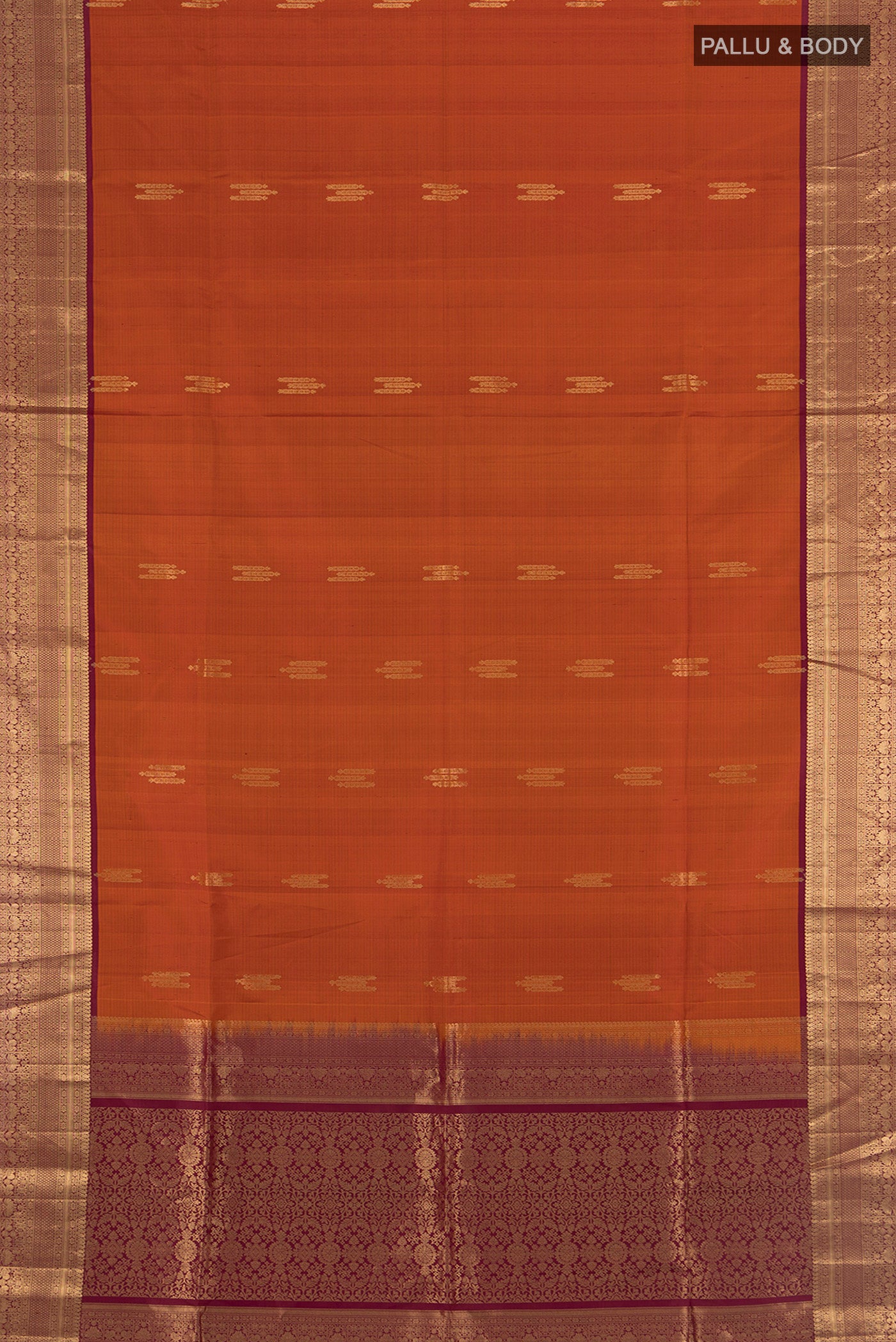 Flat view of Rust Soft Silk Saree with Zari Butta on the body and Zari Border. 