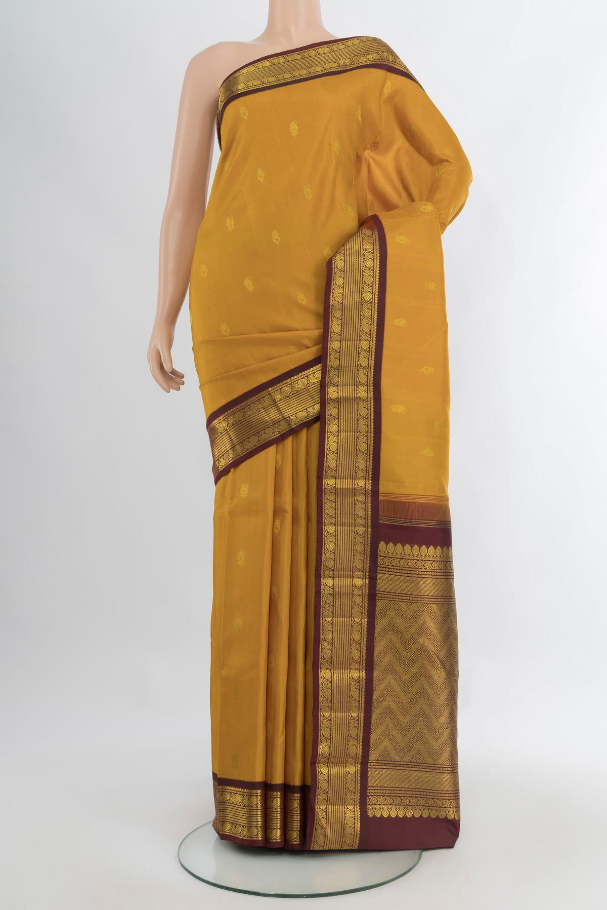 Mustard Kanchipuram Silk Saree with Zari Butta on the body and Zari Border.  displayed on a mannequin