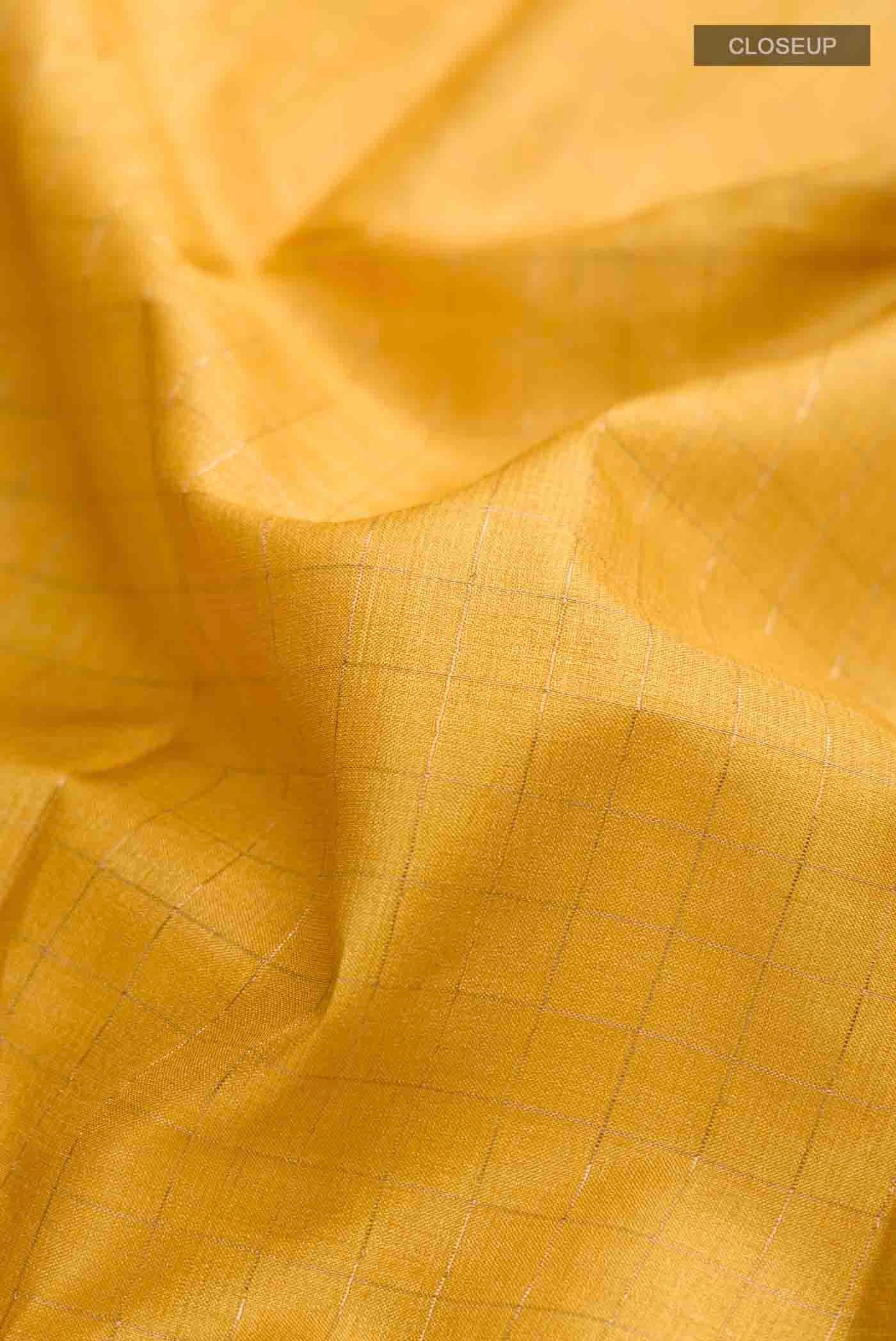 Close up of Yellow Tussar Silk Saree with Checked design on the body and Printed Border displaying folds