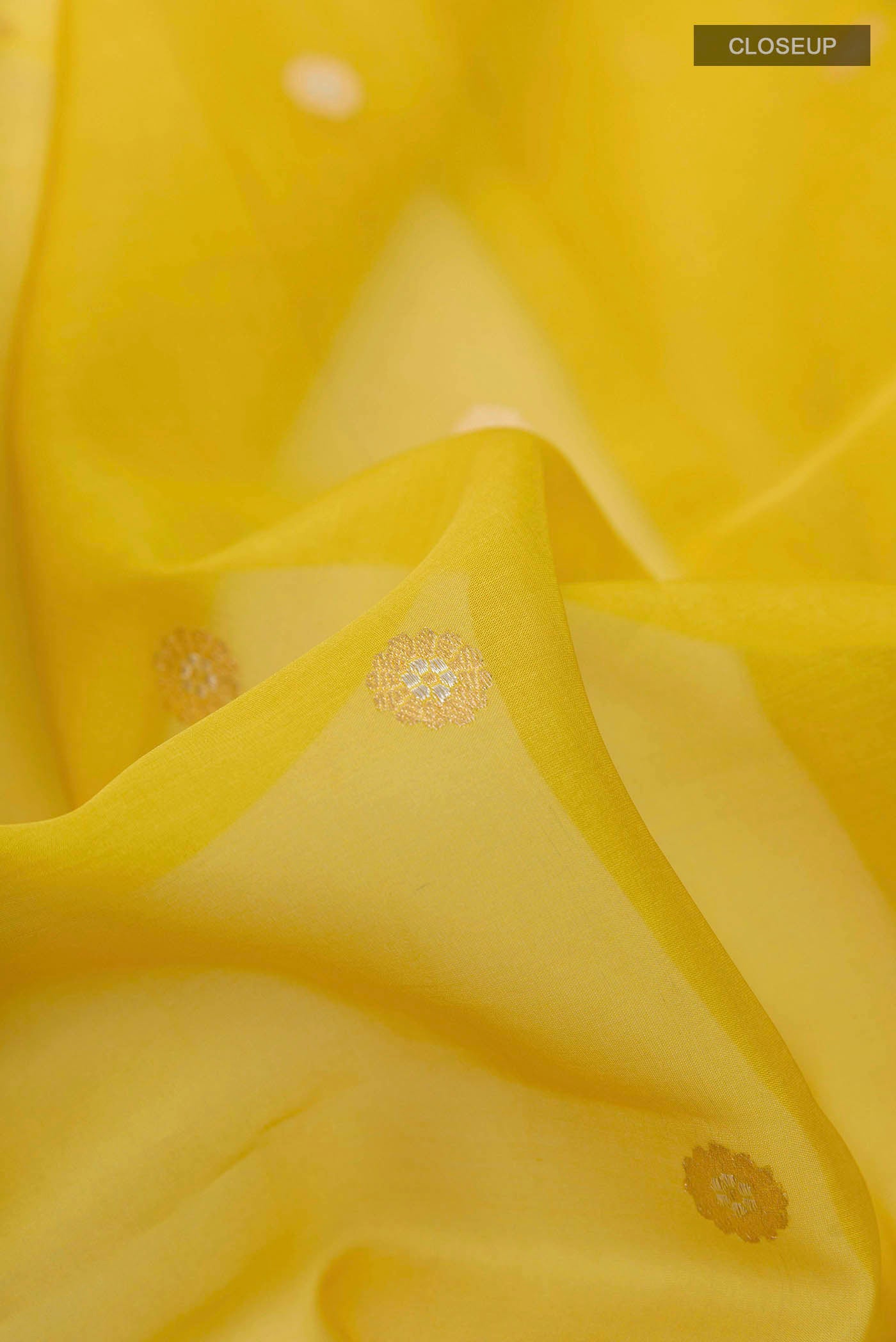Close up of Yellow Banarasi Kora Silk Saree with Zari Butta on the body and Zari Border displaying folds