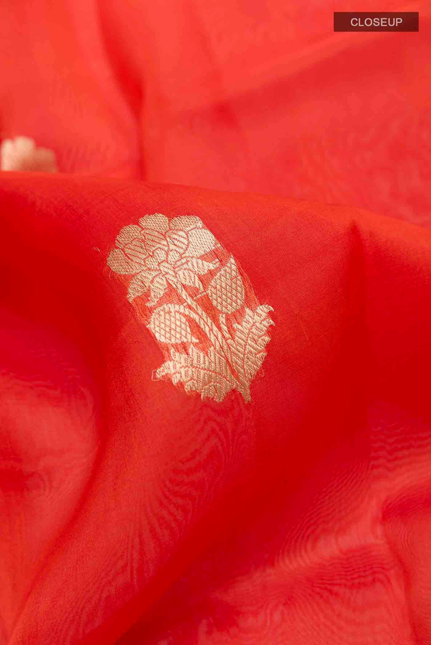 Close up of Orange Organza Silk Saree with Zari Butta on the body and Zari Border displaying folds