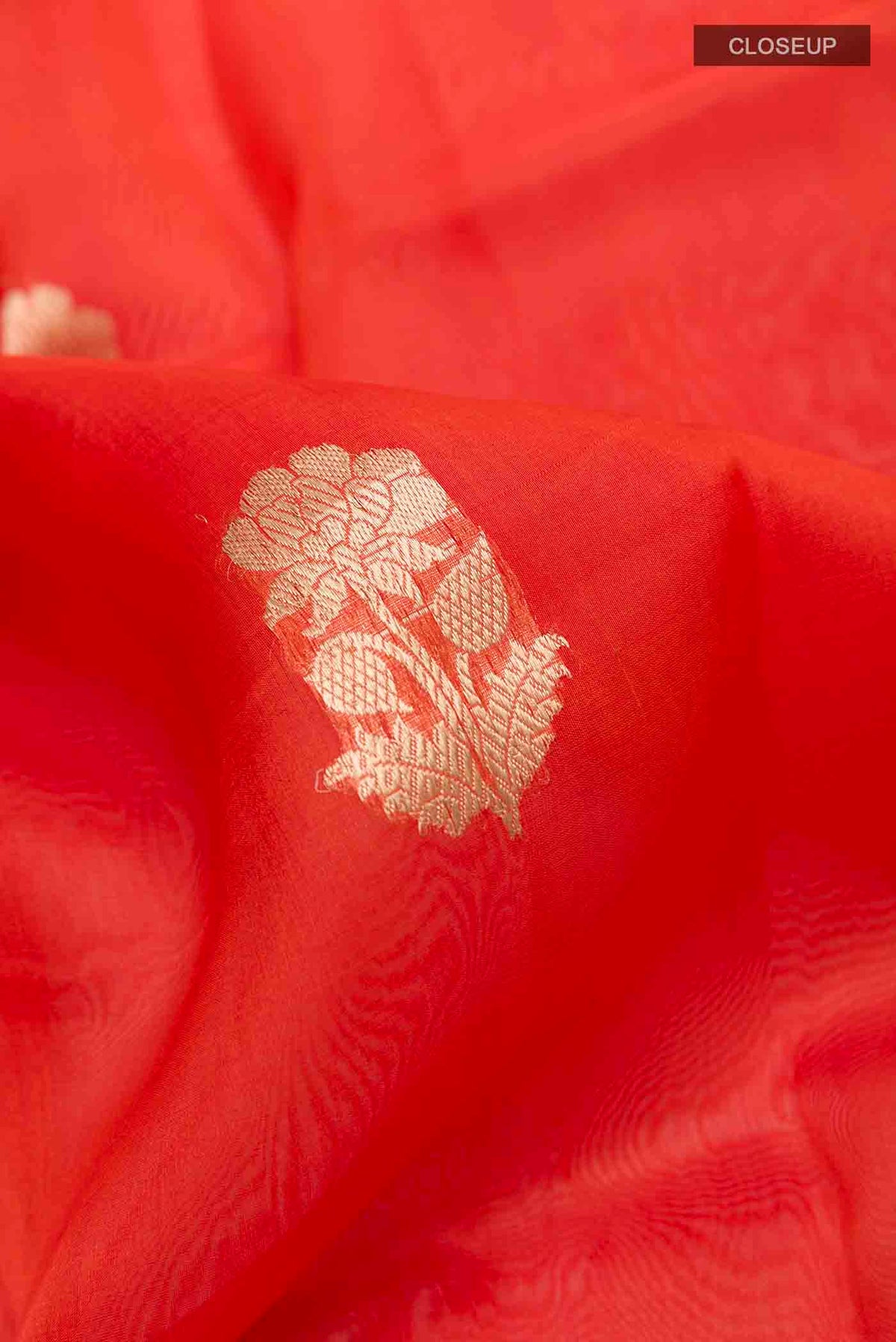Close up of Orange Organza Silk Saree with Zari Butta on the body and Zari Border displaying folds