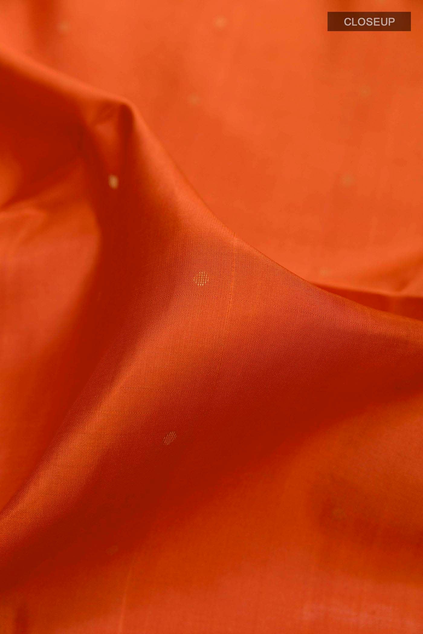Close up of Orange Soft Silk Saree with Zari Butta on the body and Zari Border displaying folds