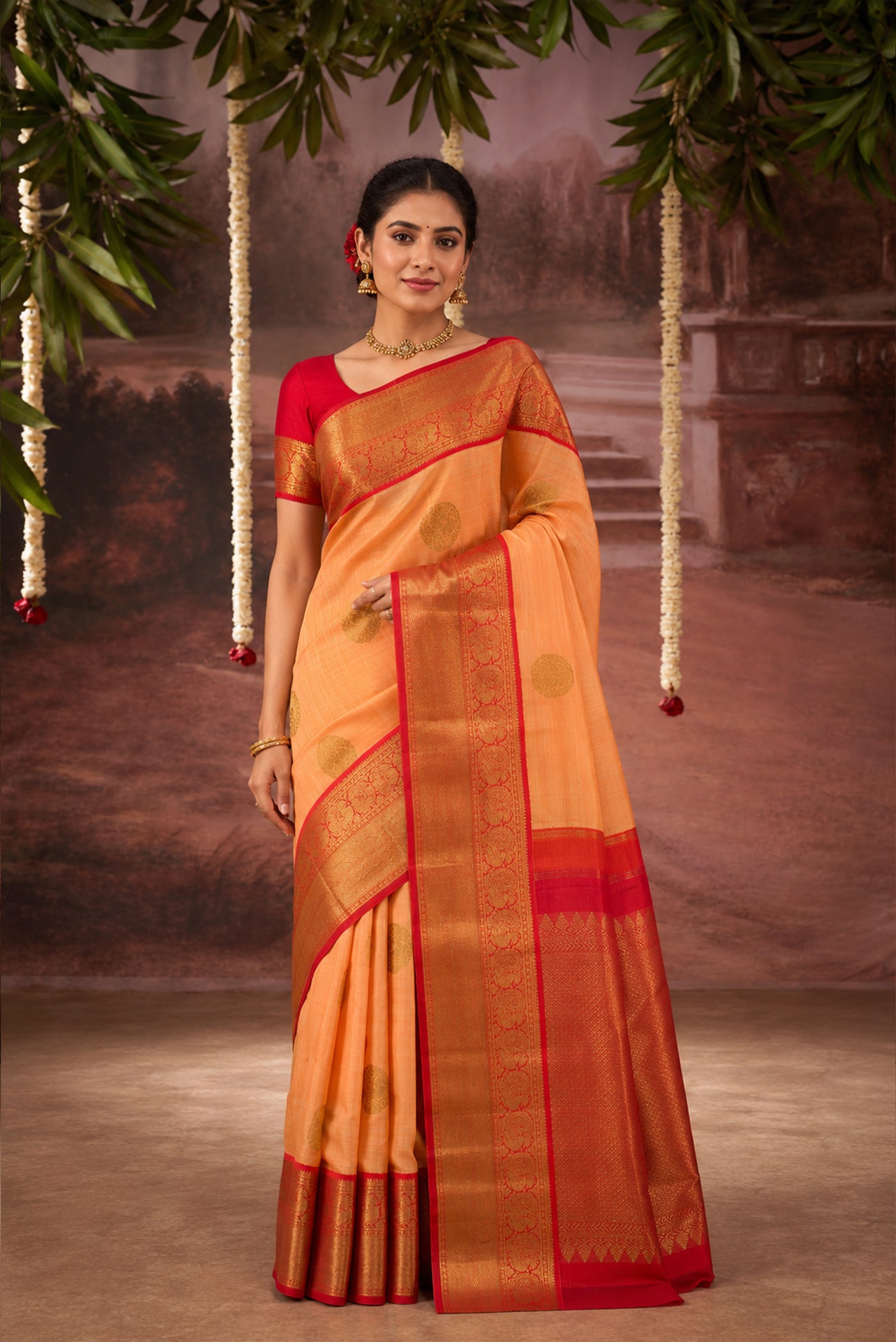 Model wearing a Orange Kanchipuram Silk Saree with Zari Butta on the body and Zari Border.