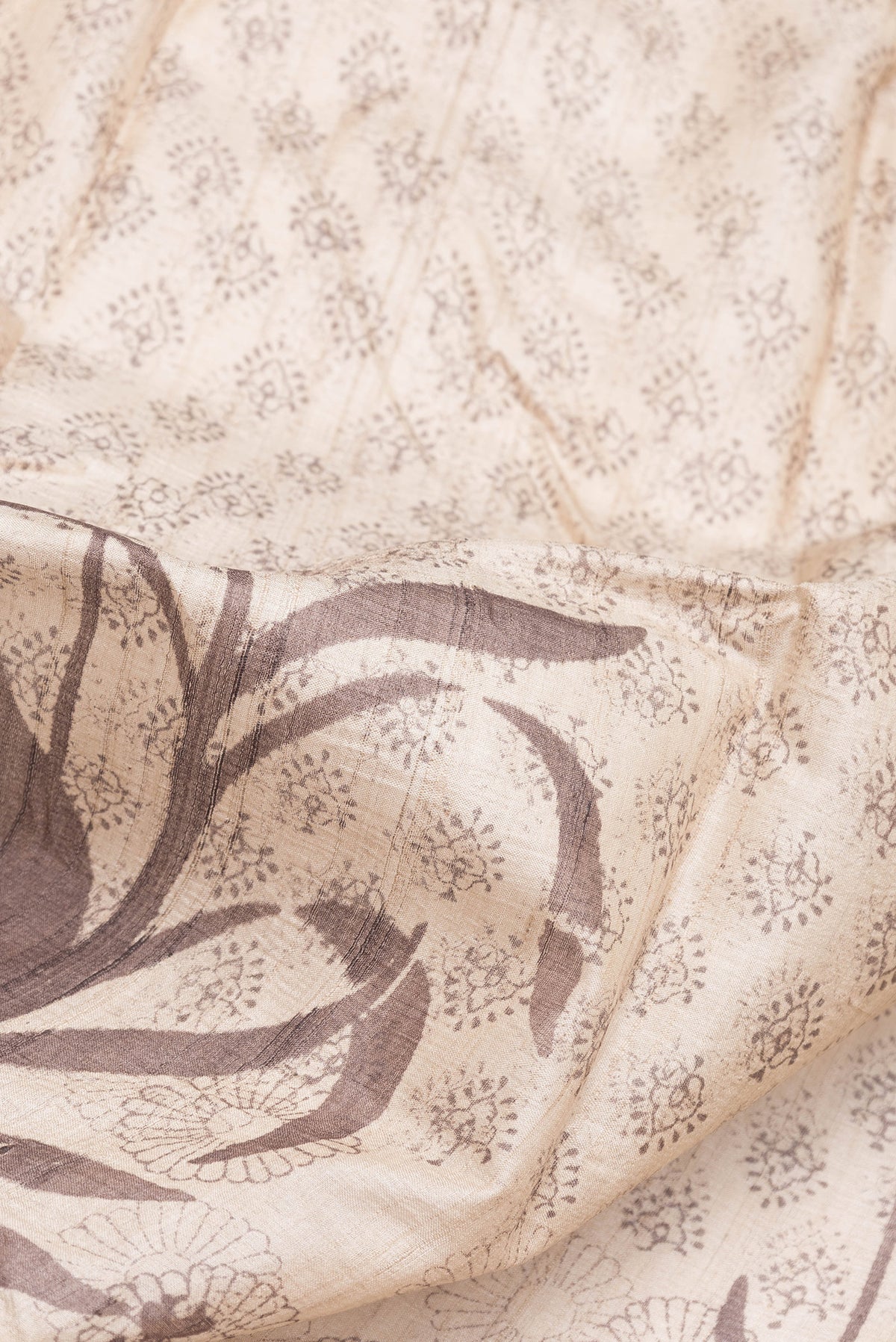 Close up of Beige Tussar Silk Saree with Printed design on the body and Fancy Border.  displaying folds