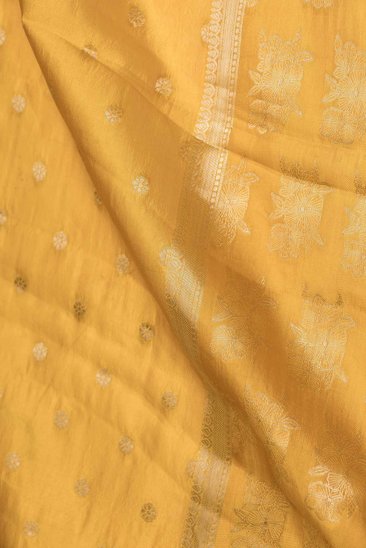 Close up of Yellow Banarasi Raw Silk Saree with Zari Butta on the body and Zari Border displaying folds