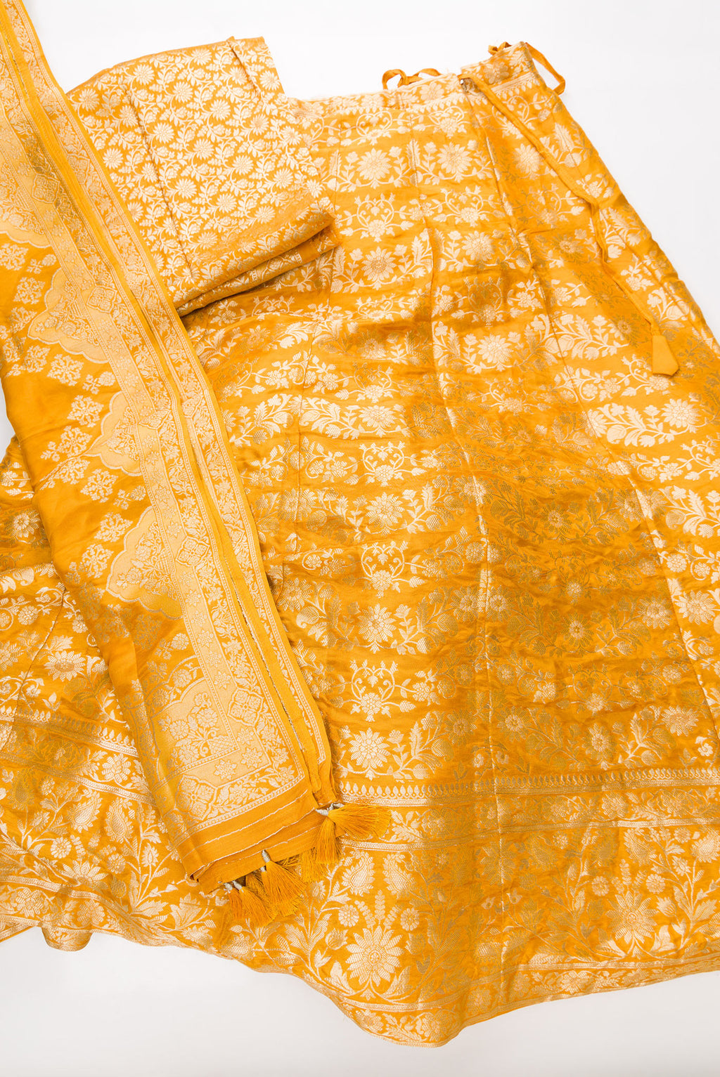 Flat lay of Mustard Banarasi Silk Womens Lehenga set featuring Zari Brocade Choli paired with Mustard Zari Brocade Skirt with Zari Border and a Zari Brocade dupatta in Mustard