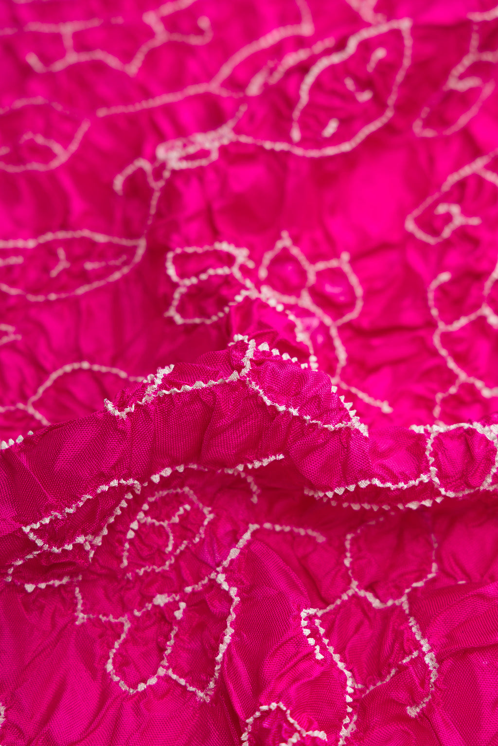 Close up of Pink Dual Tone Bandhani Silk Saree with Bandhani Print on the body and Ikat Border.  displaying folds