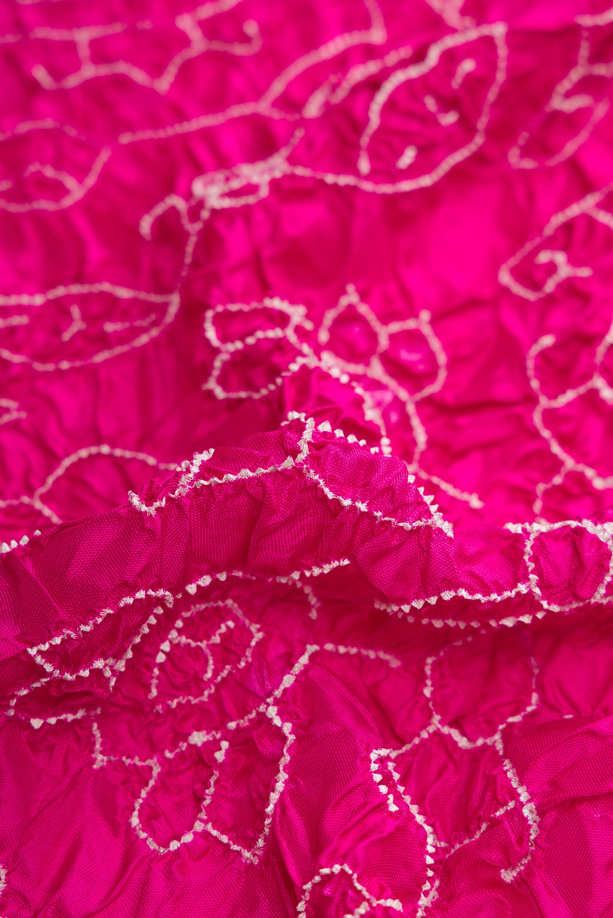 Close up of Pink Dual Tone Bandhani Silk Saree with Bandhani Print on the body and Ikat Border.  displaying folds
