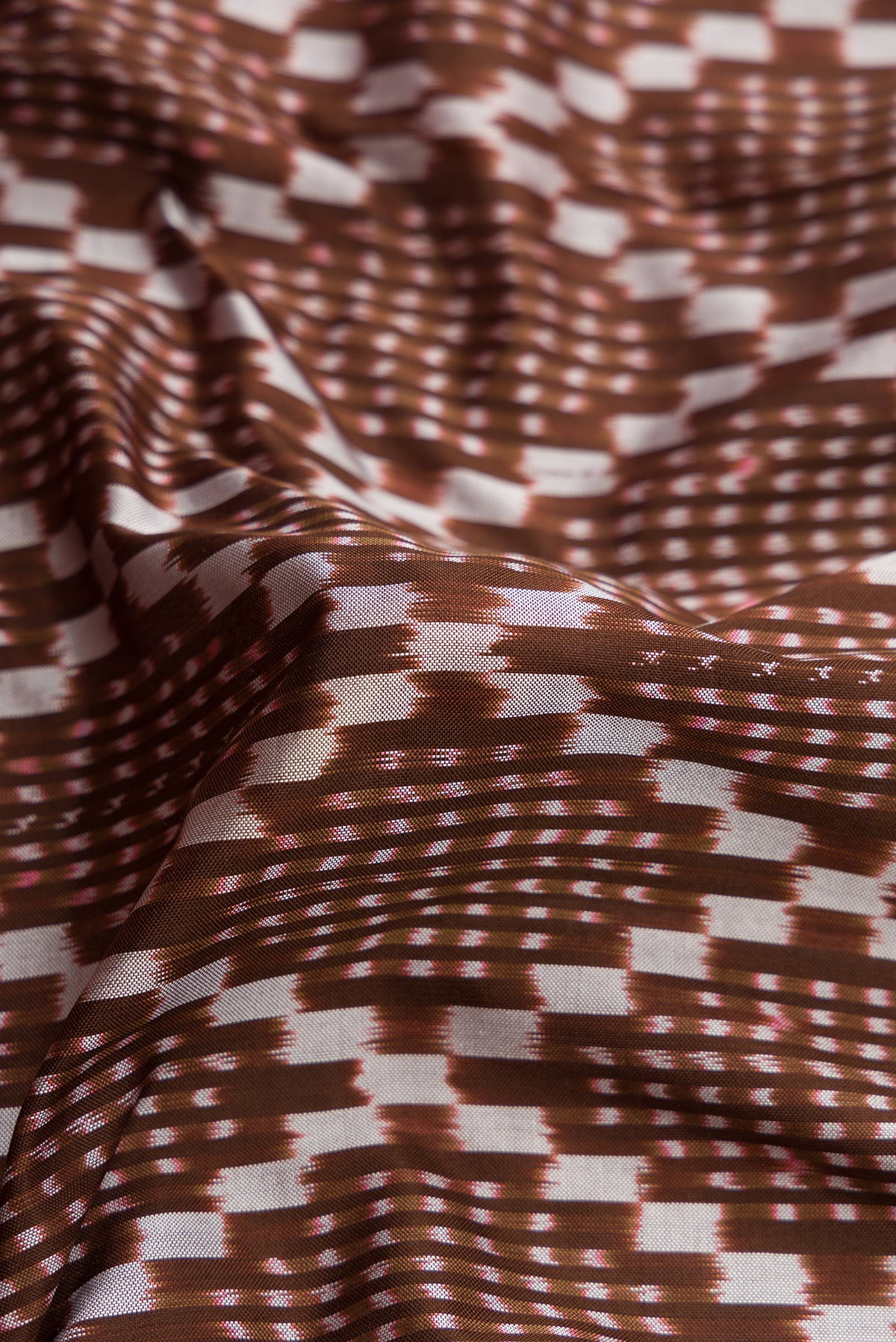 Close up of Brown Dual Tone Double Ikat Saree with Ikat Print on the body and Zari Border.  displaying folds