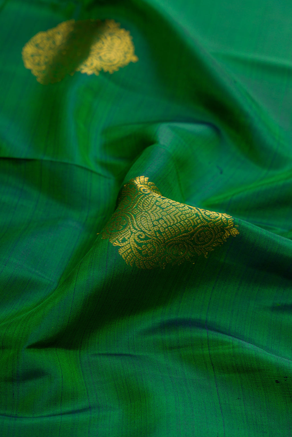 Close up of Green Dual Tone Kanjivaram Silk Saree with Zari Butta on the body and Zari Border.  displaying folds