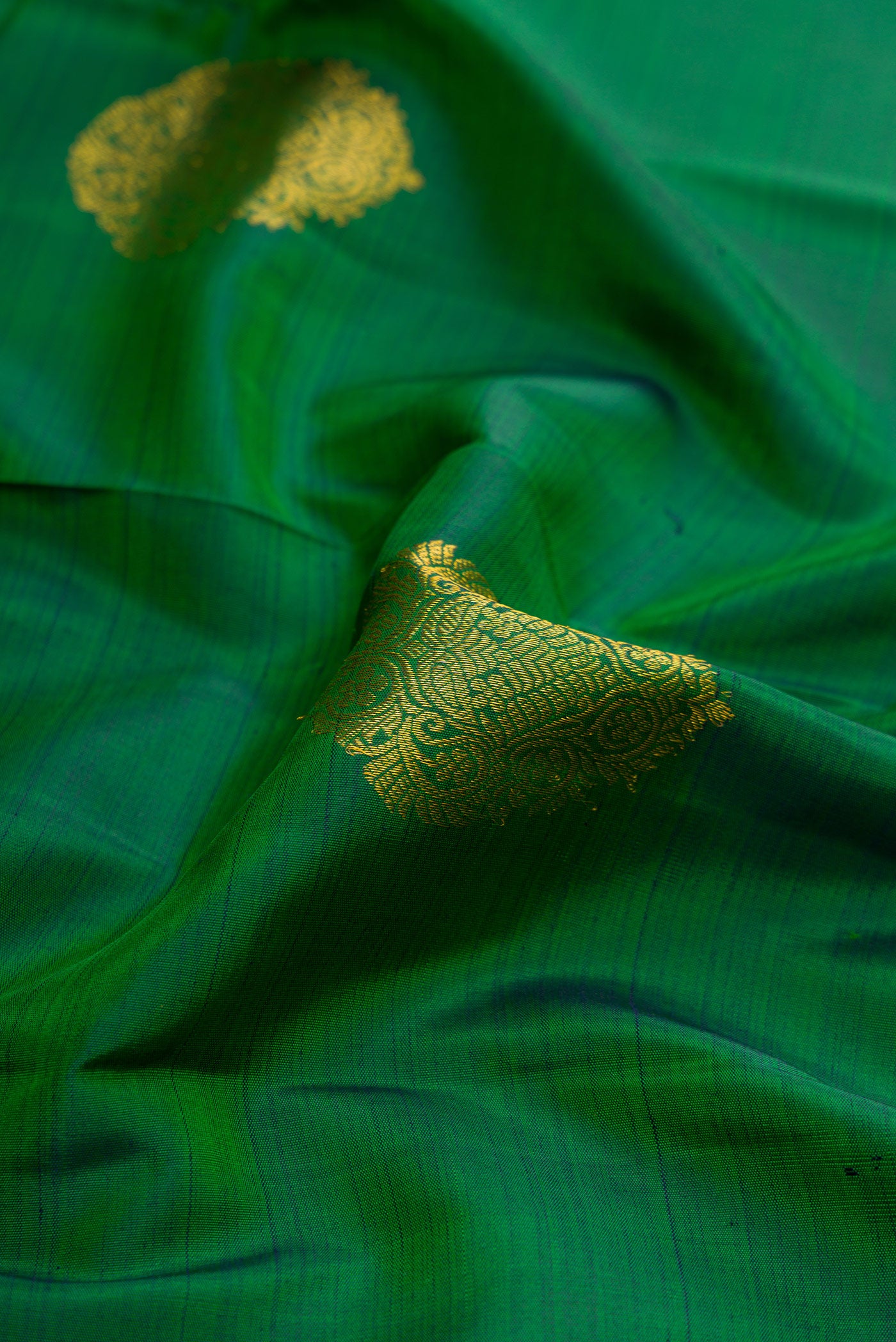Close up of Green Dual Tone Kanjivaram Silk Saree with Zari Butta on the body and Zari Border.  displaying folds