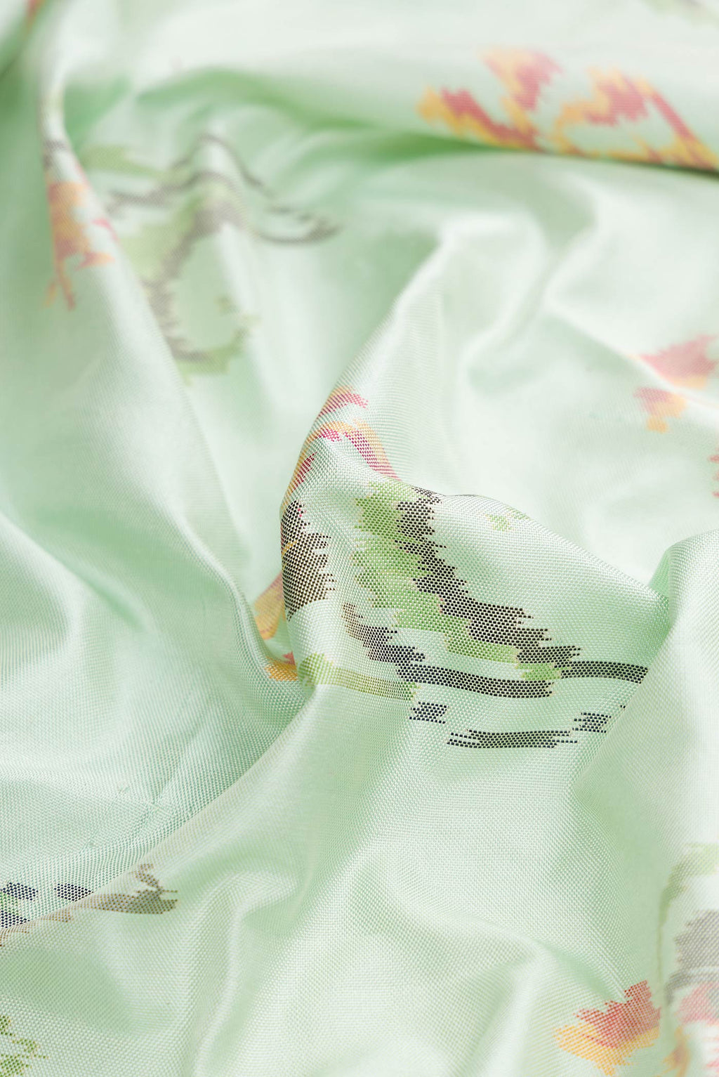 Close up of Light Green Dual Tone Double Ikat Saree with Ikat Print on the body and Zari And Thread Border displaying folds