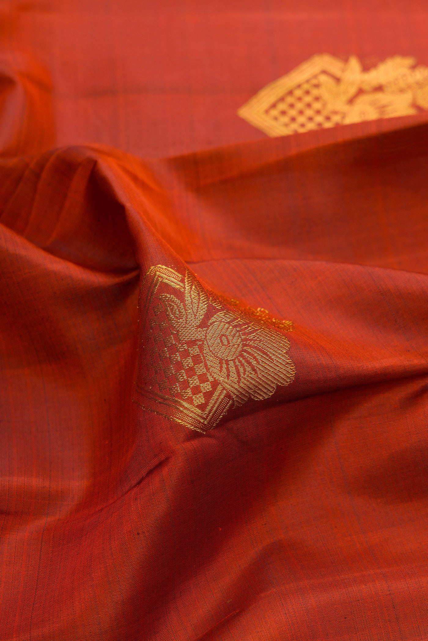 Close up of Brick Orange Kanjivaram Silk Saree with Zari Butta on the body and Zari Border.  displaying folds
