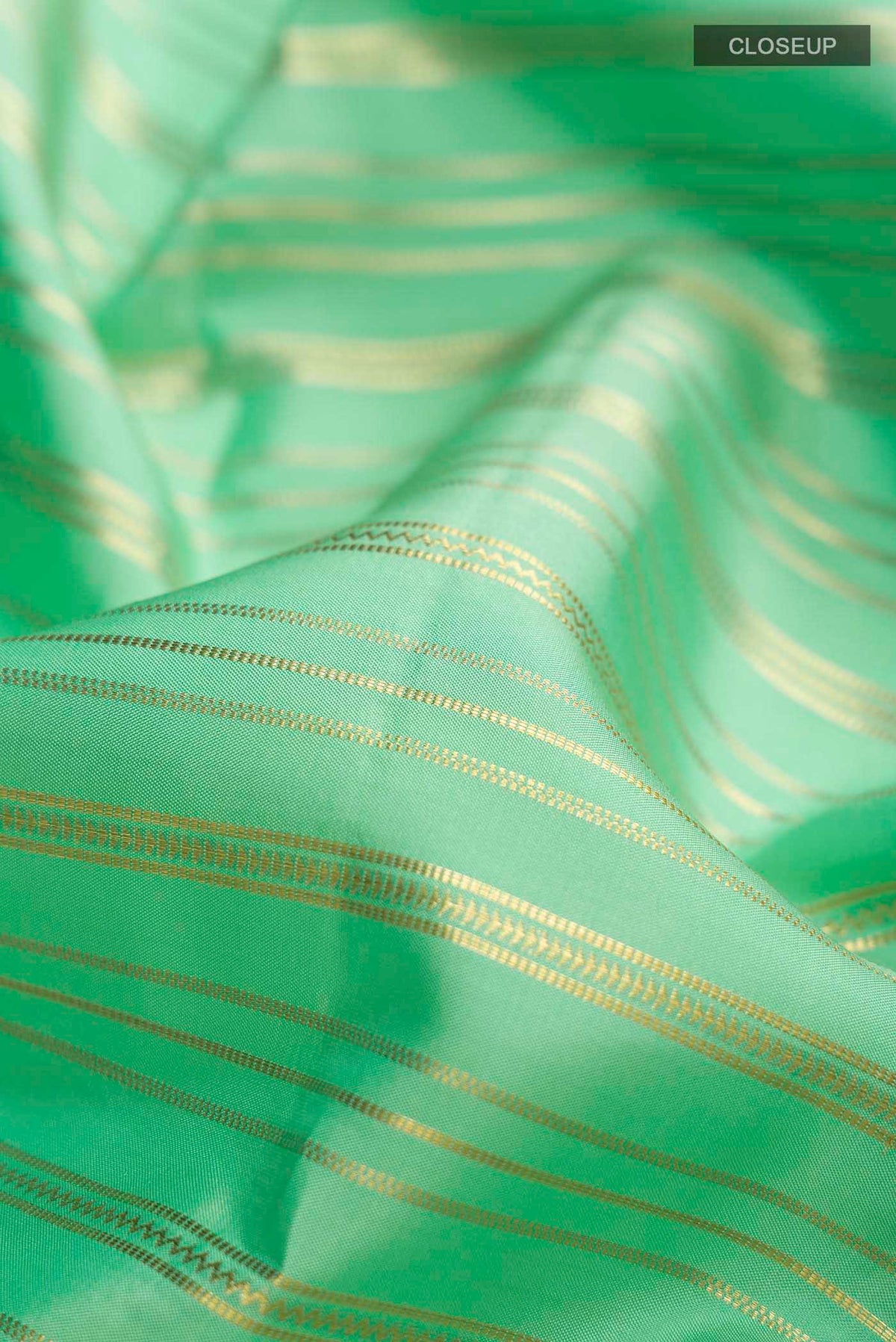 Close up of Green Kanchipuram Silk Saree with Stripes on the body and Zari Border displaying folds