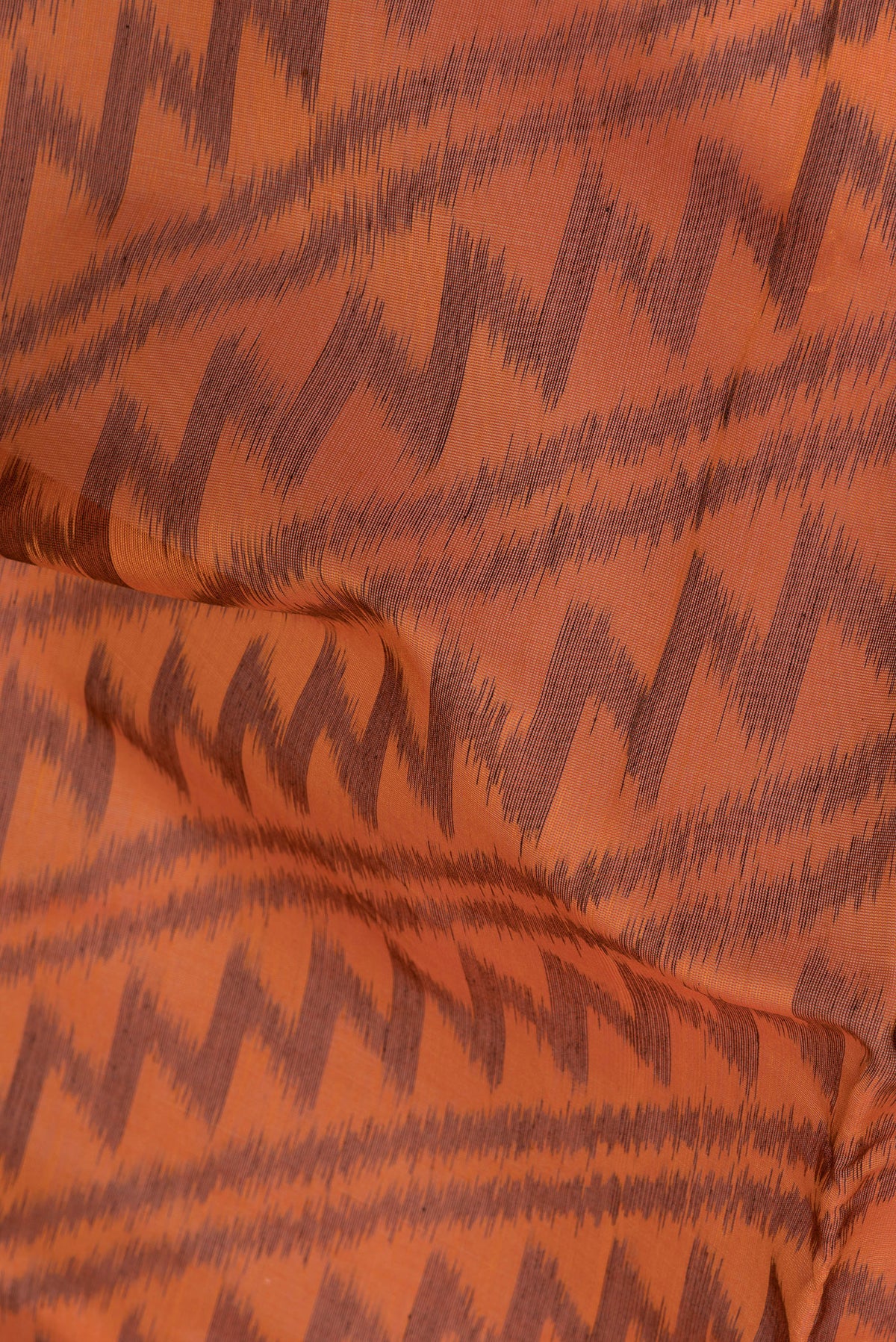 Close up of Orange Silk Cotton Saree with Ikat Print on the body and Ikat Border.  displaying folds