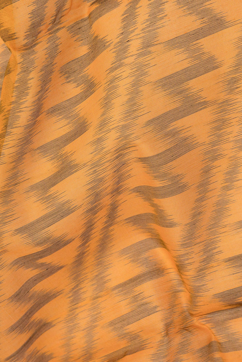 Close up of Orange Silk Cotton Saree with Ikat Print on the body and Zari Border.  displaying folds