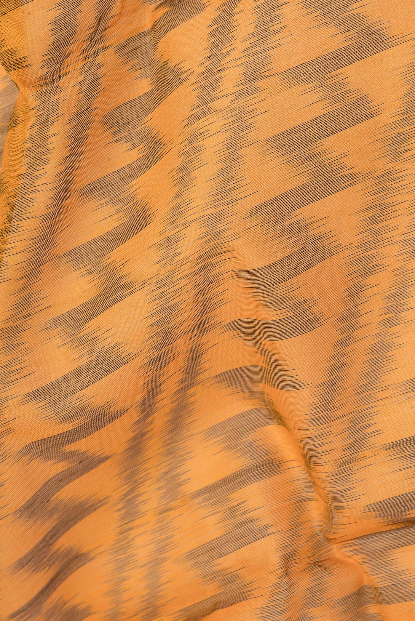 Close up of Orange Silk Cotton Saree with Ikat Print on the body and Zari Border.  displaying folds