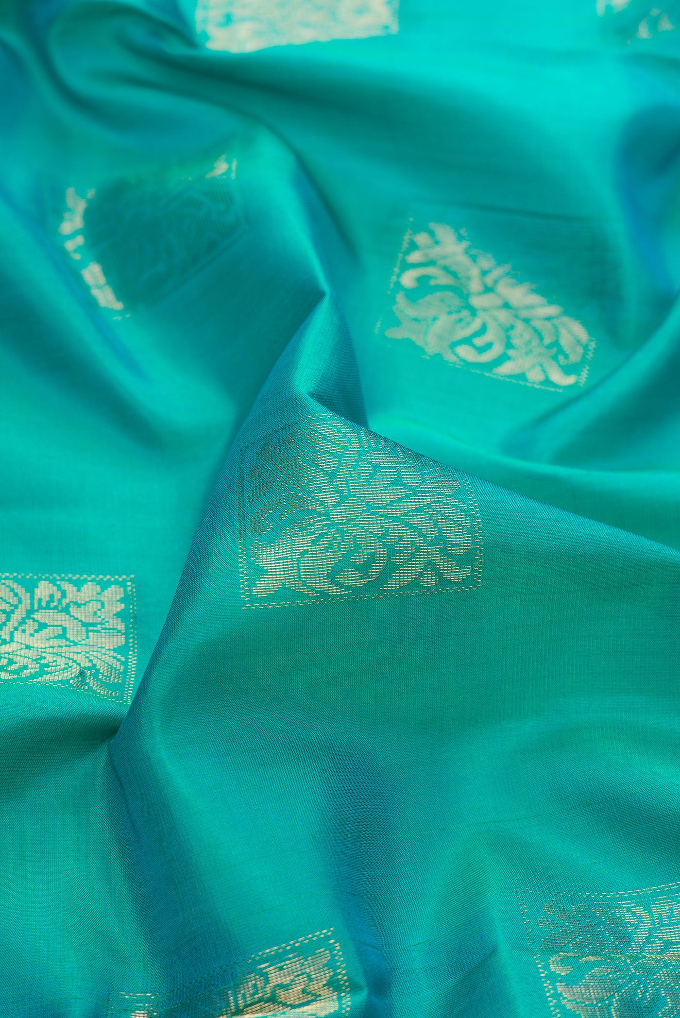 Close up of Peacock Blue Dual Tone Soft Silk Saree with Zari Butta on the body and Fancy Border.  displaying folds