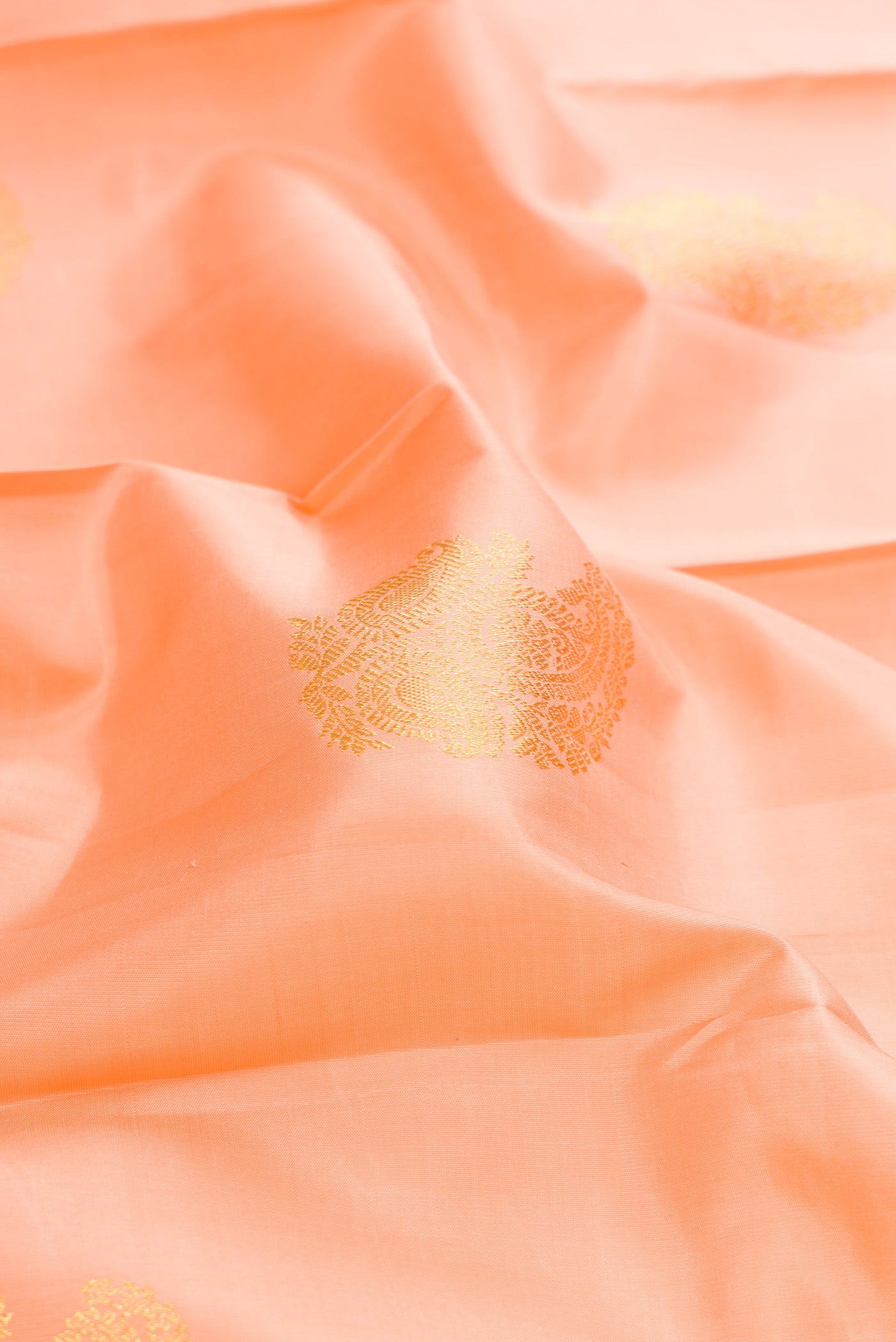 Close up of Peach Dual Tone Kanjivaram Silk Saree with Zari Butta on the body and Zari Border.  displaying folds