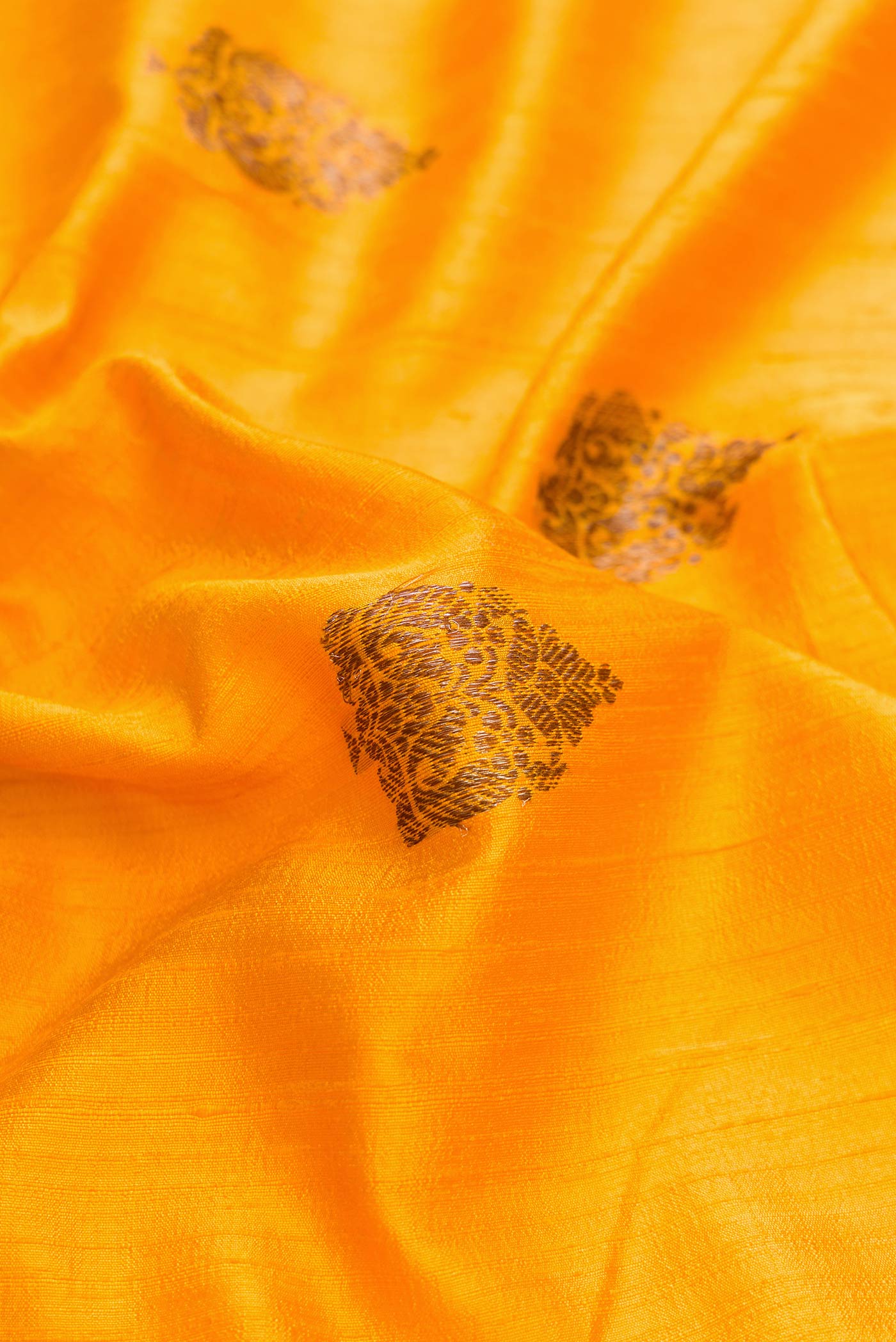 Close up of Mustard Dual Tone Raw Silk Saree with Zari Butta on the body and Zari Border displaying folds