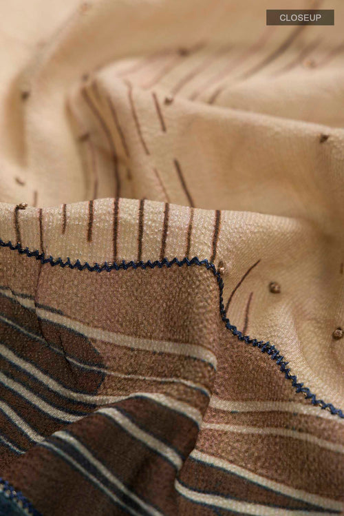Close up of Beige Tussar Silk Saree with Embroidery on the body and Zari Border displaying folds
